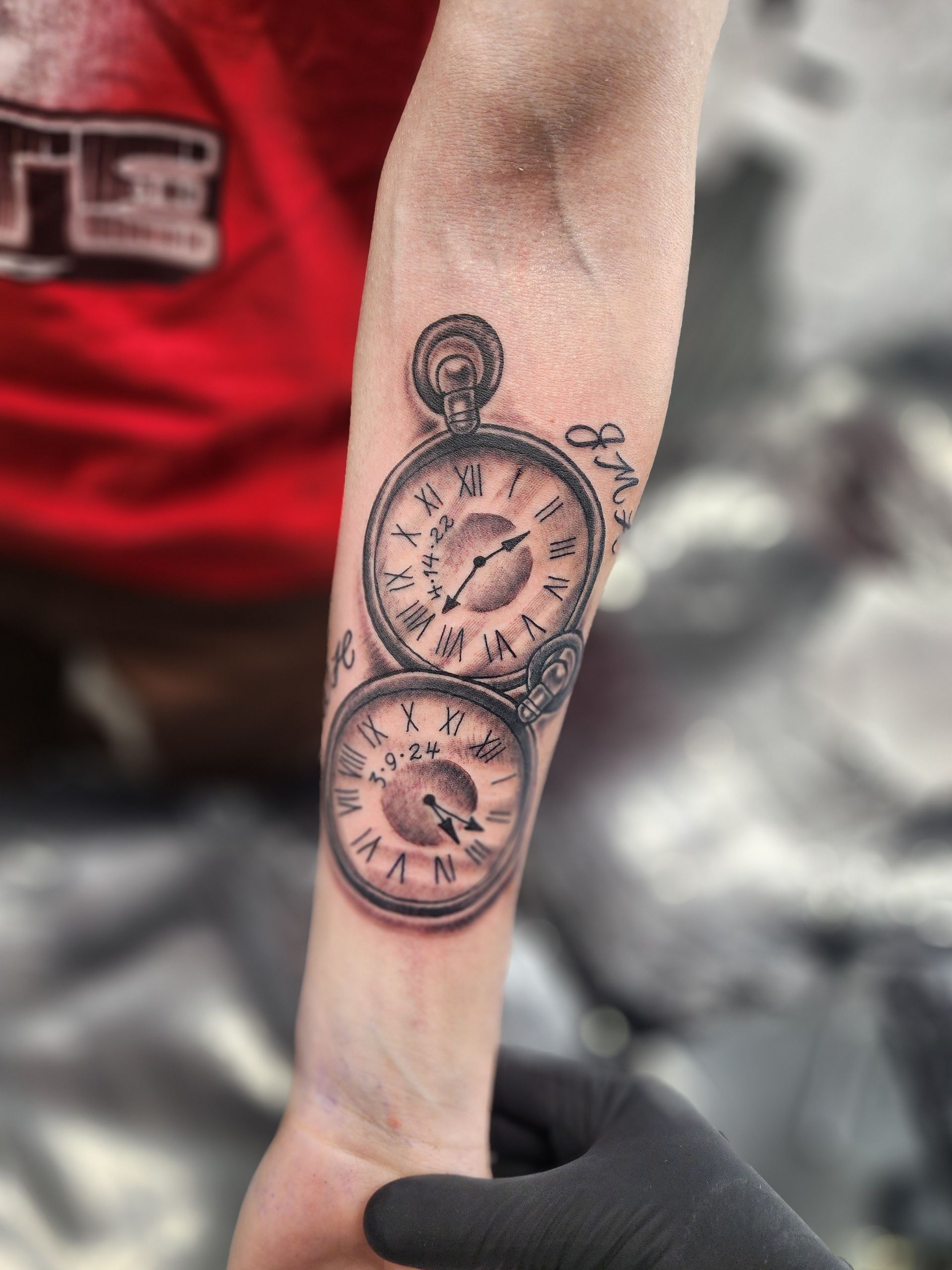 Tattoo of two pocket watches on a forearm. One watch is above the other. Black gloves hold the arm.
