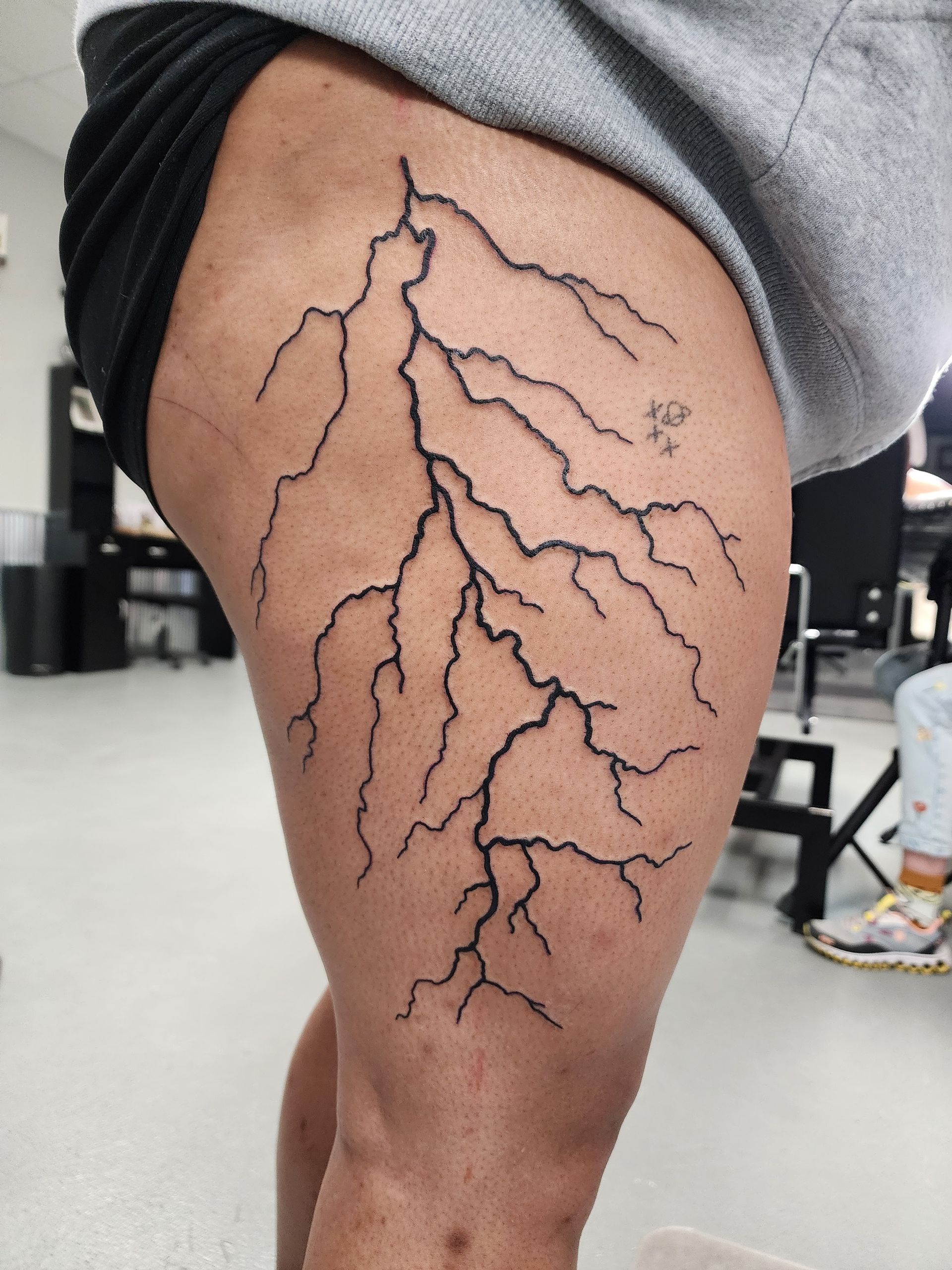 Lightning bolt tattoo on a person's thigh, black ink, in a studio setting.