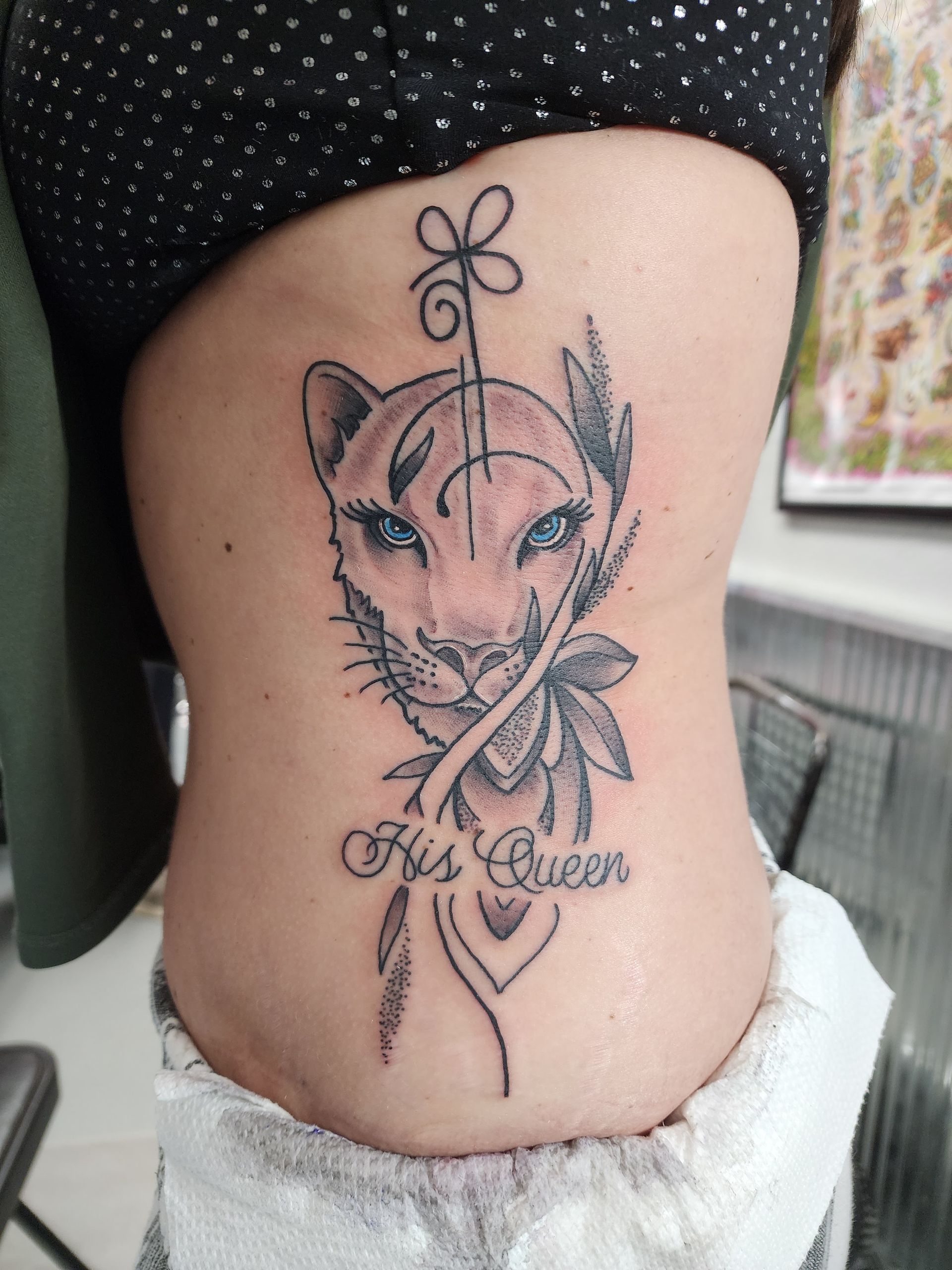 Tattoo of a panther-like face with blue eyes and floral accents on a person's side, text