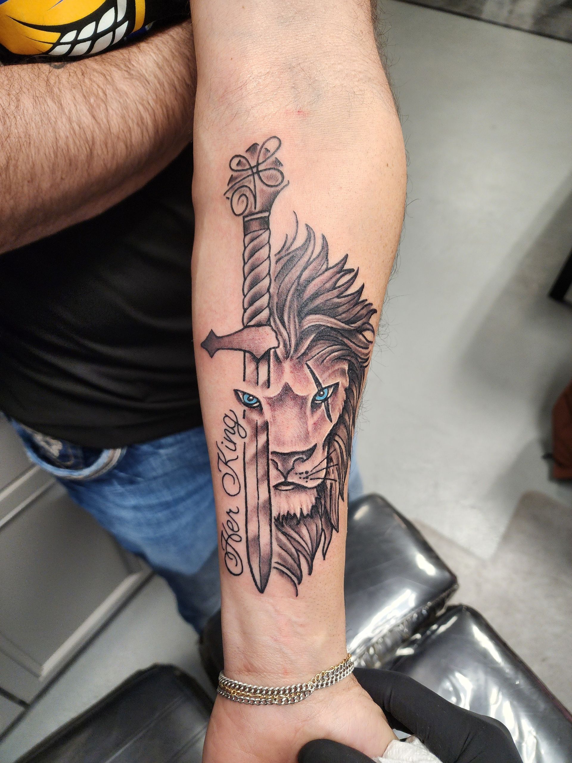 Tattoo of a lion's face pierced by a sword on a forearm.