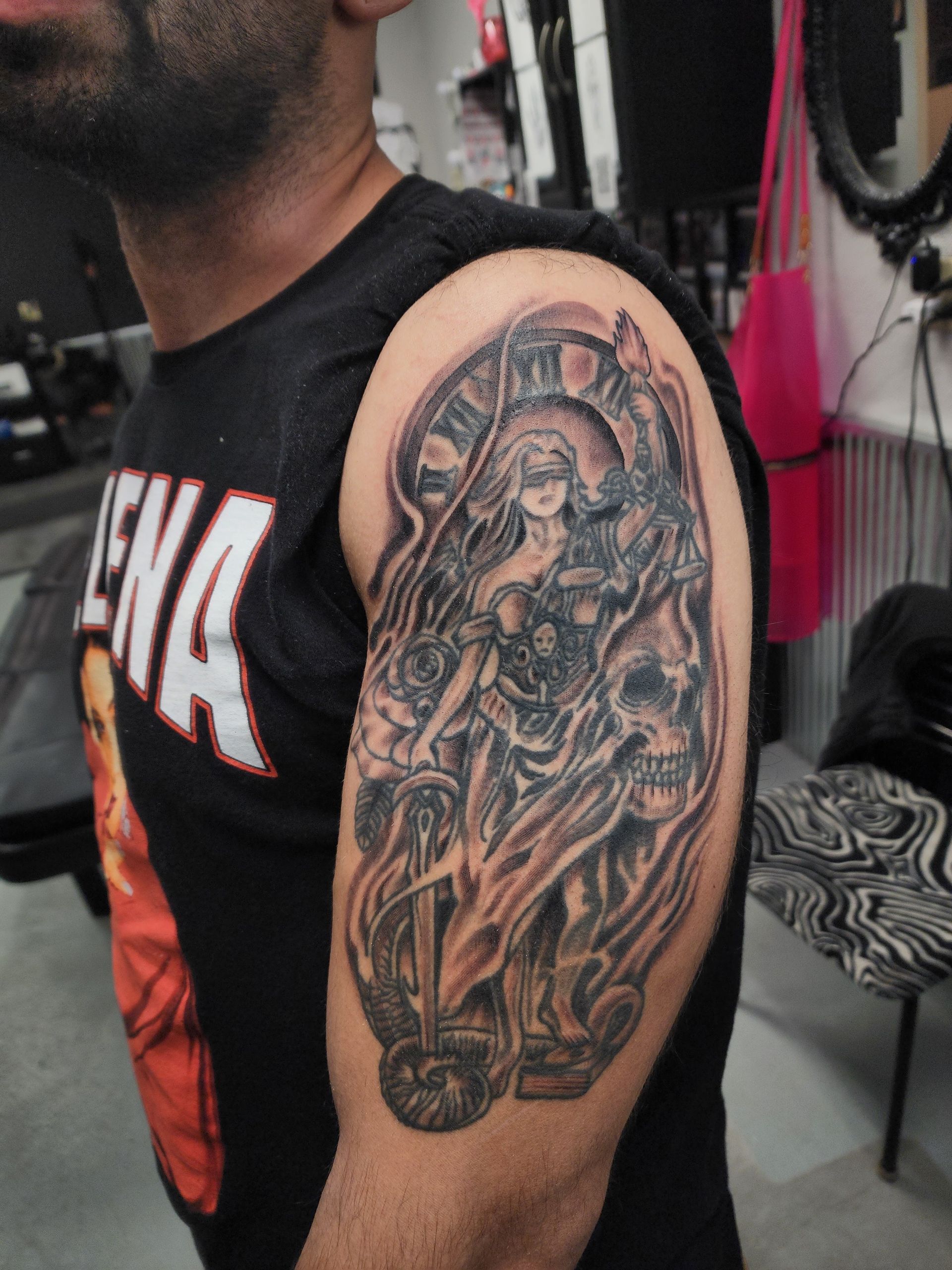 Tattoo of a robed woman with a blindfold holding a sword, with scales and a skull on arm.