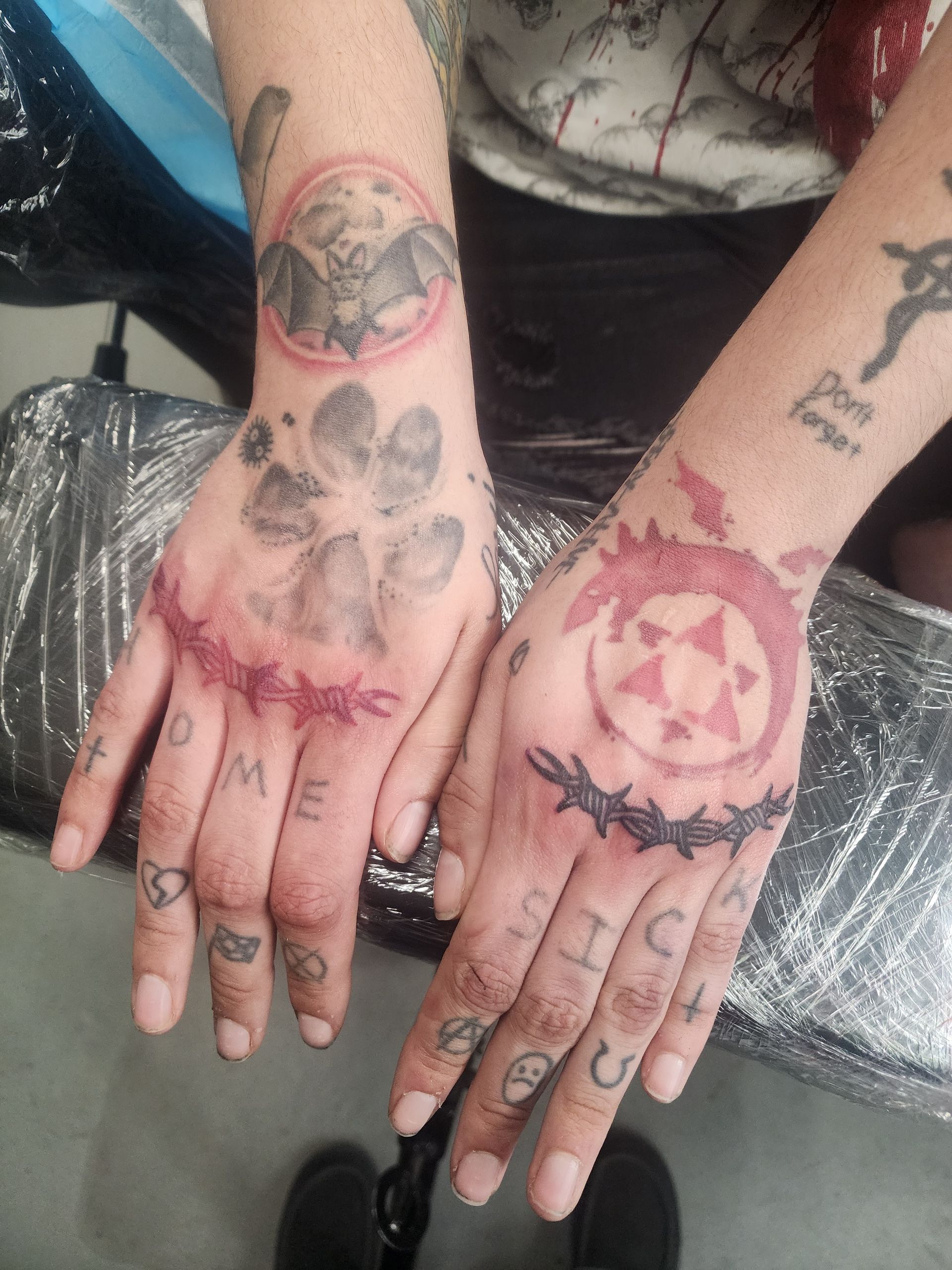 Tattooed hands with various designs: paw prints, a symbol, barbed wire, and lettering.