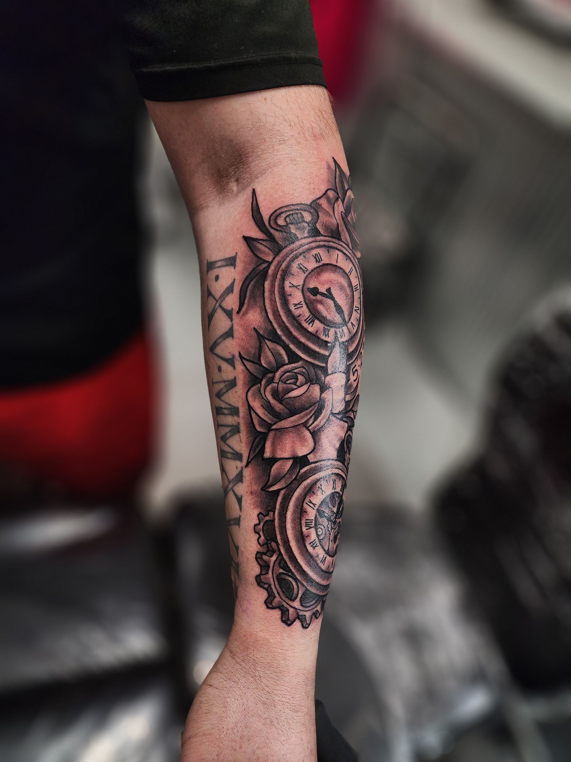 Tattoo on a forearm with gears, roses, and Roman numerals. Black and white ink.