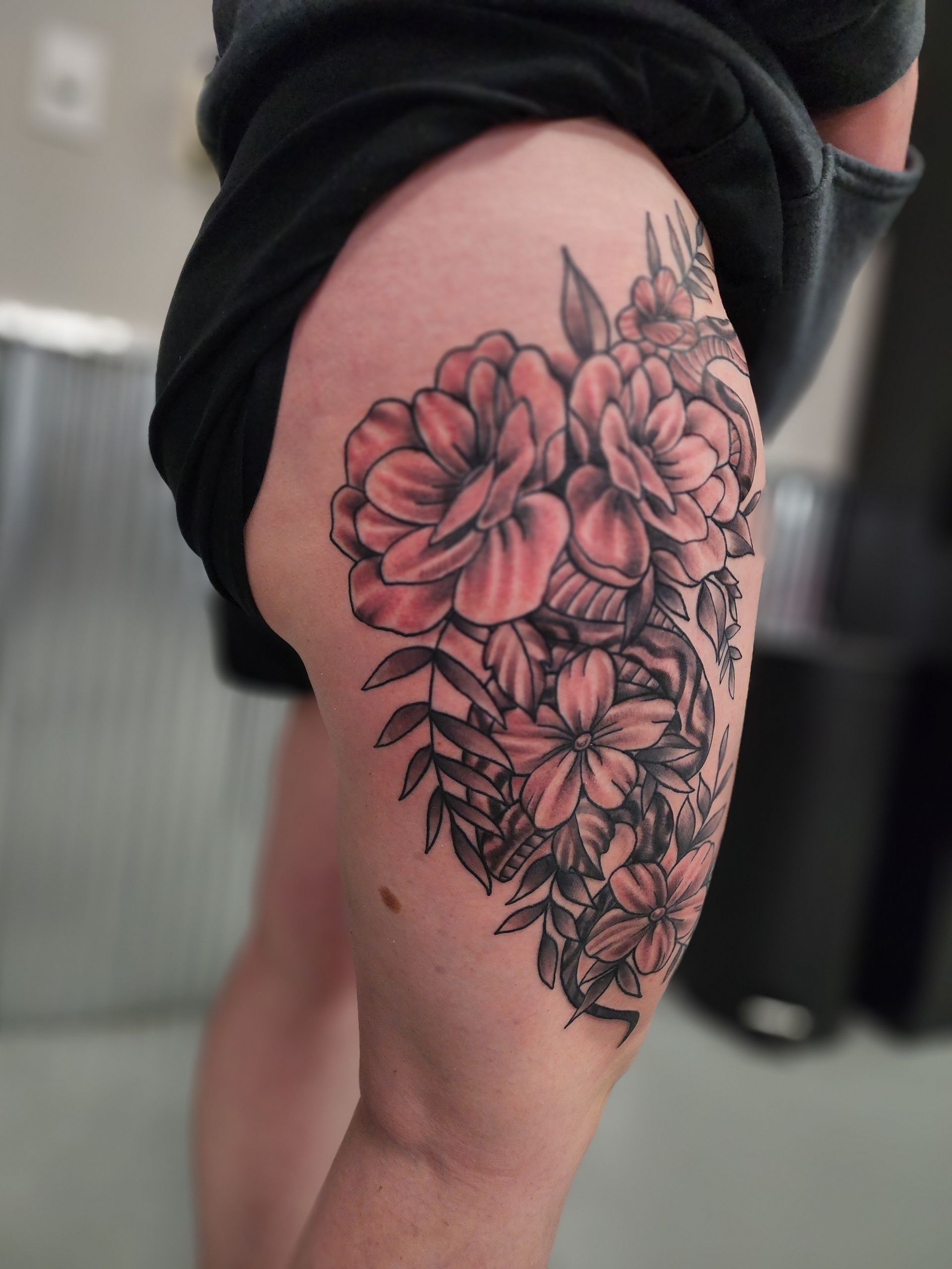 Tattoo of large floral arrangement on a person's thigh, black and gray shading with some red.