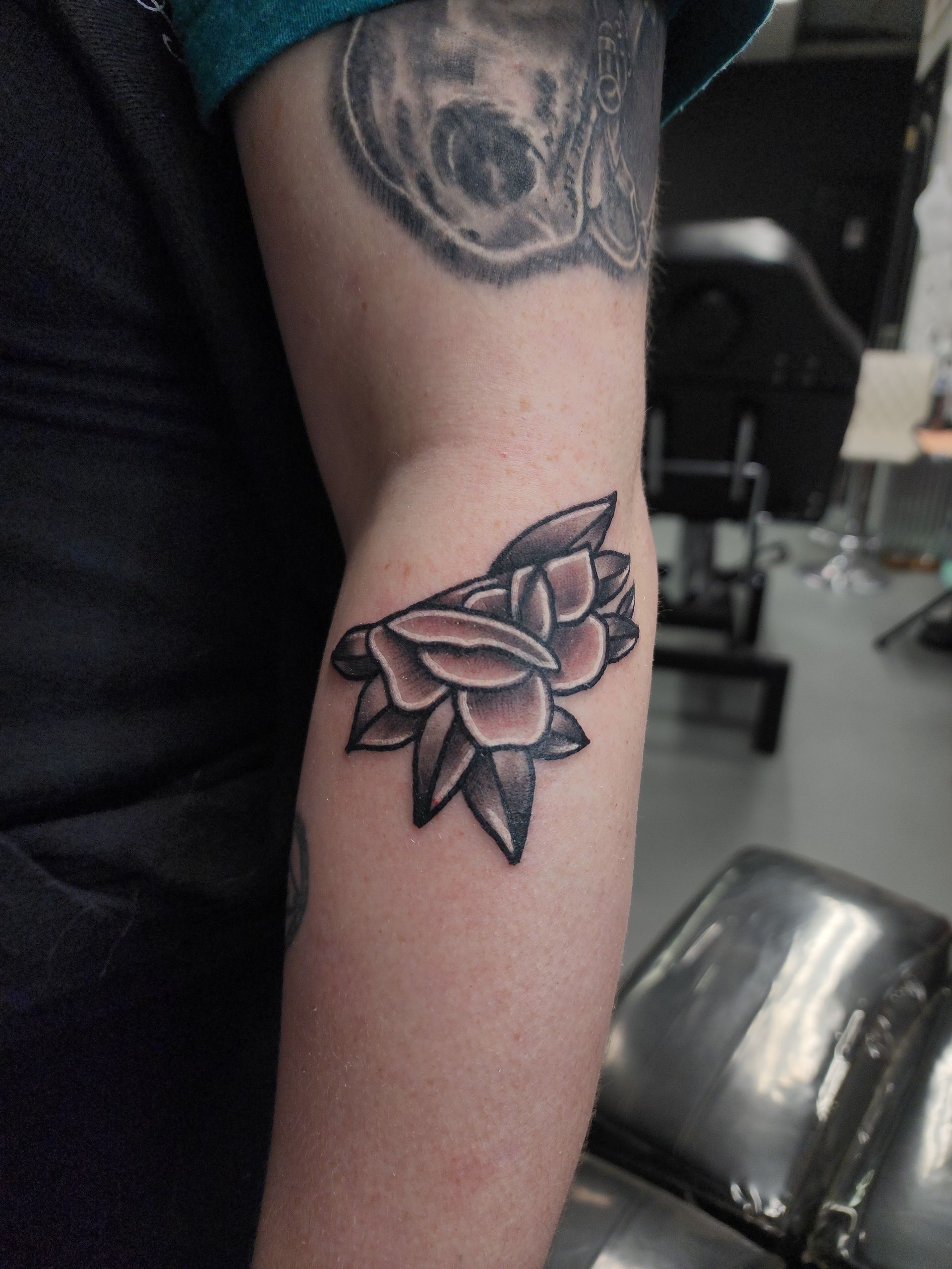 Tattoo of a shaded flower on a person's inner elbow, with dark petals and leaves.