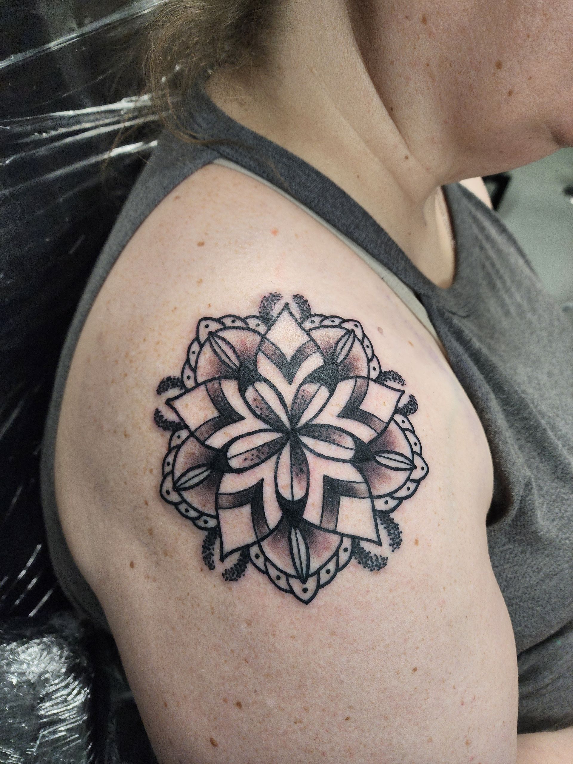 Black and gray floral mandala tattoo on a person's shoulder, outlined in black ink.