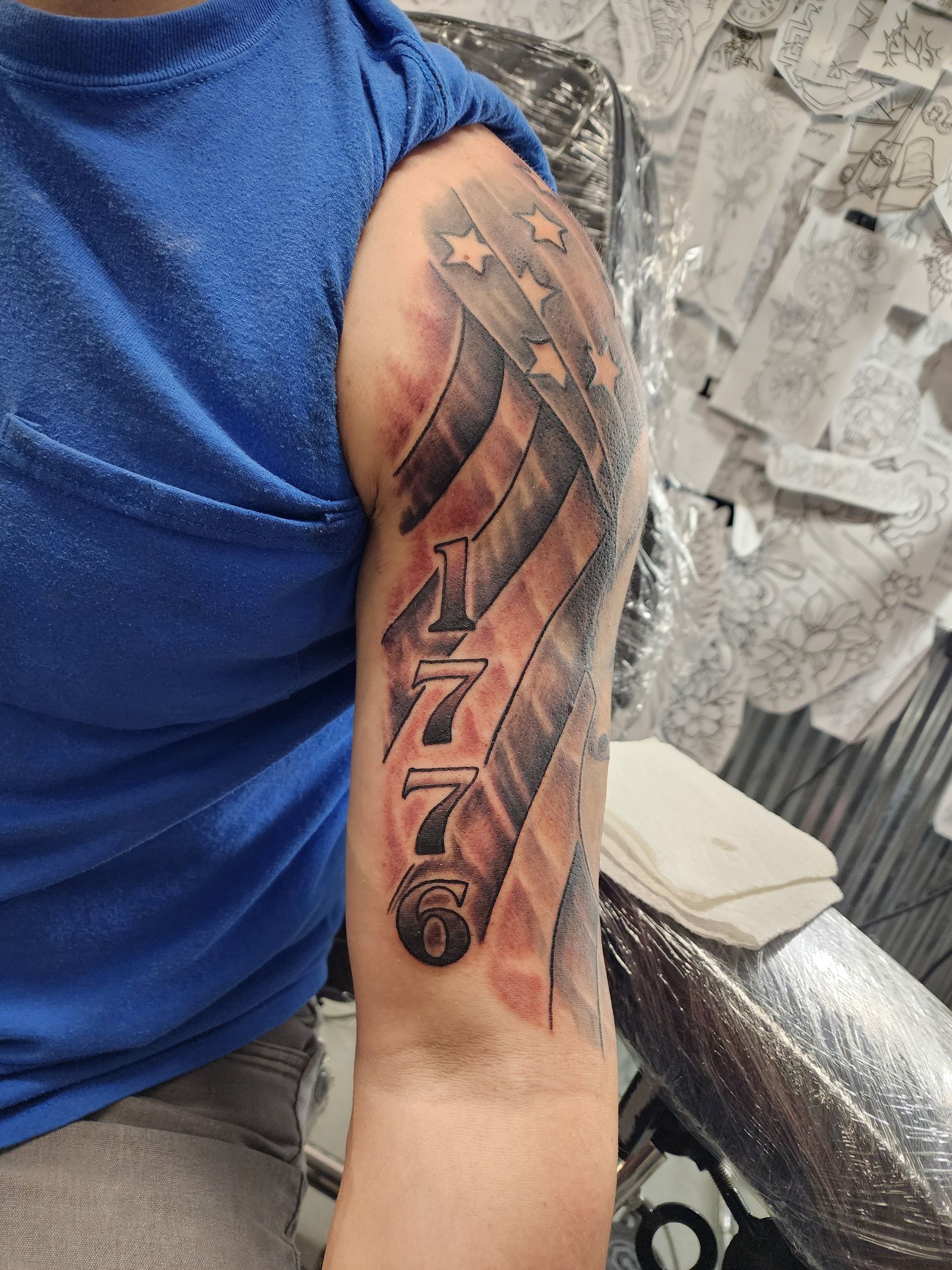 Tattoo of the American flag on a person's upper arm, with the year 1776 in the middle.
