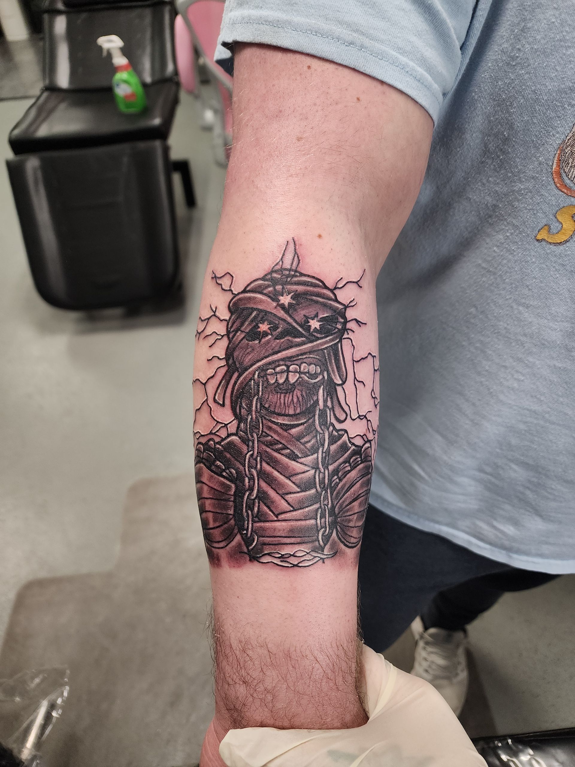 Tattoo of a mummy on a person's forearm, black and gray ink, wrapped in bandages.