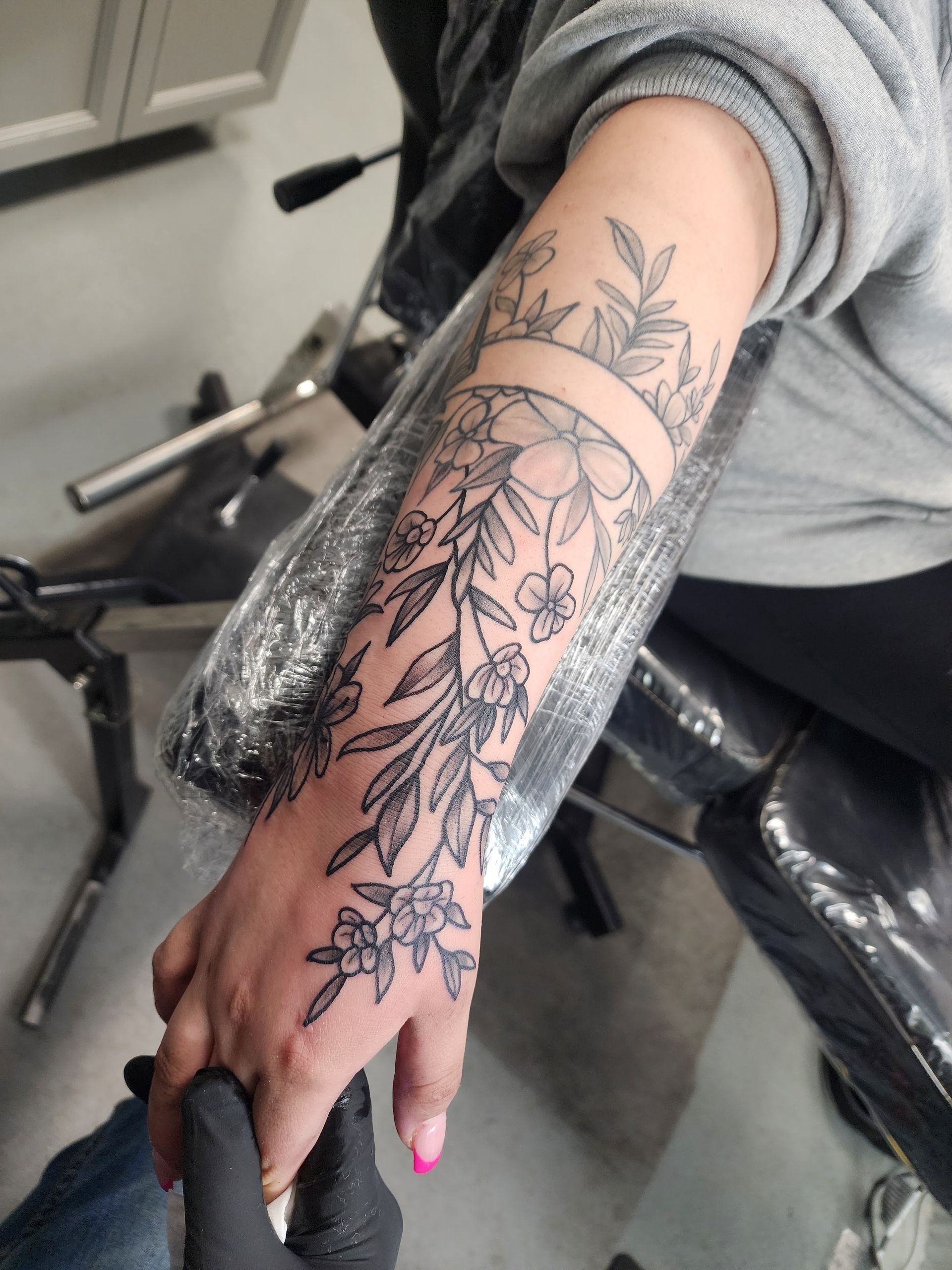 Floral tattoo on forearm and hand, being held by gloved hand.