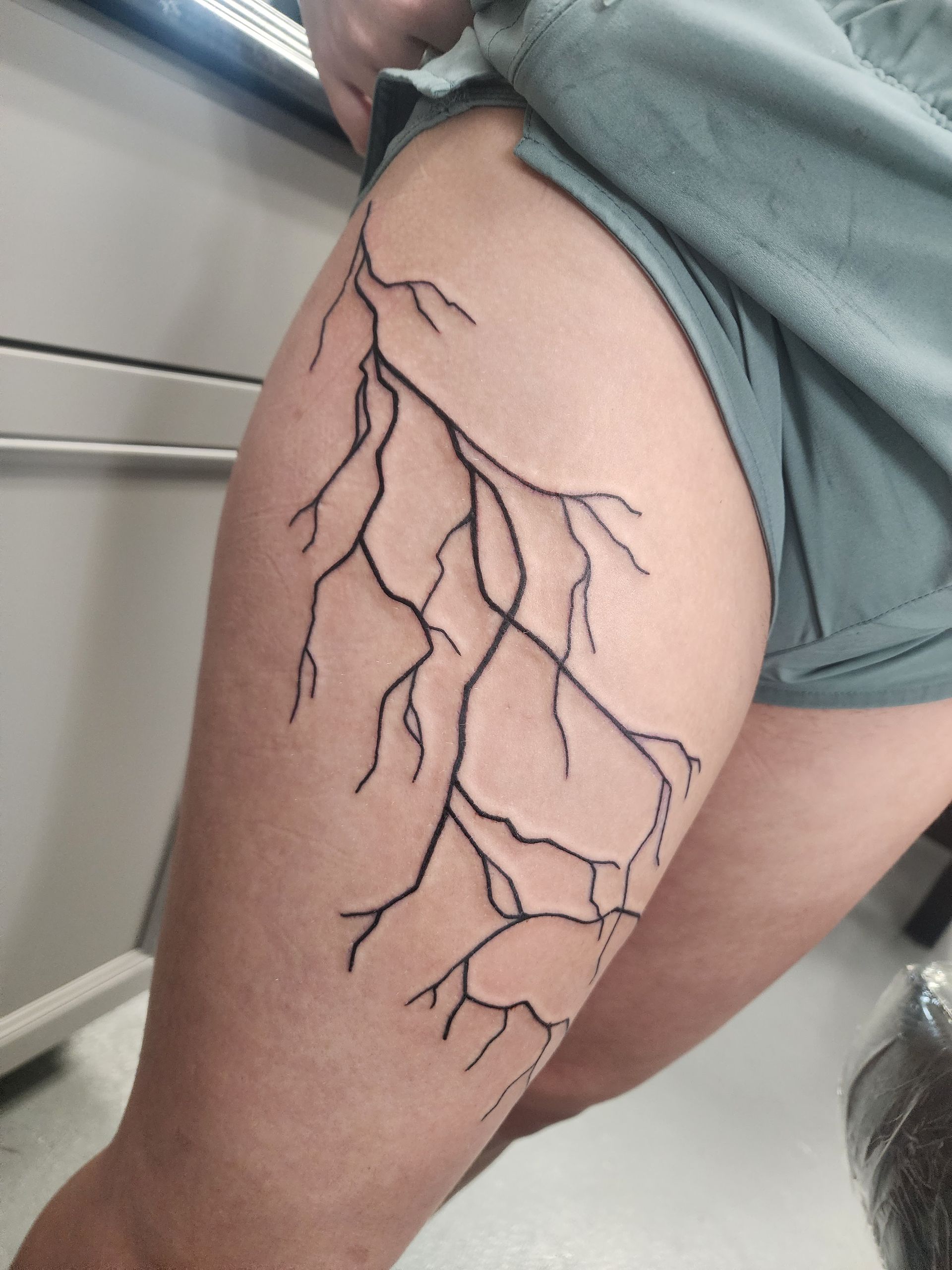 Black linework tattoo of a lightning bolt pattern on a person's thigh.