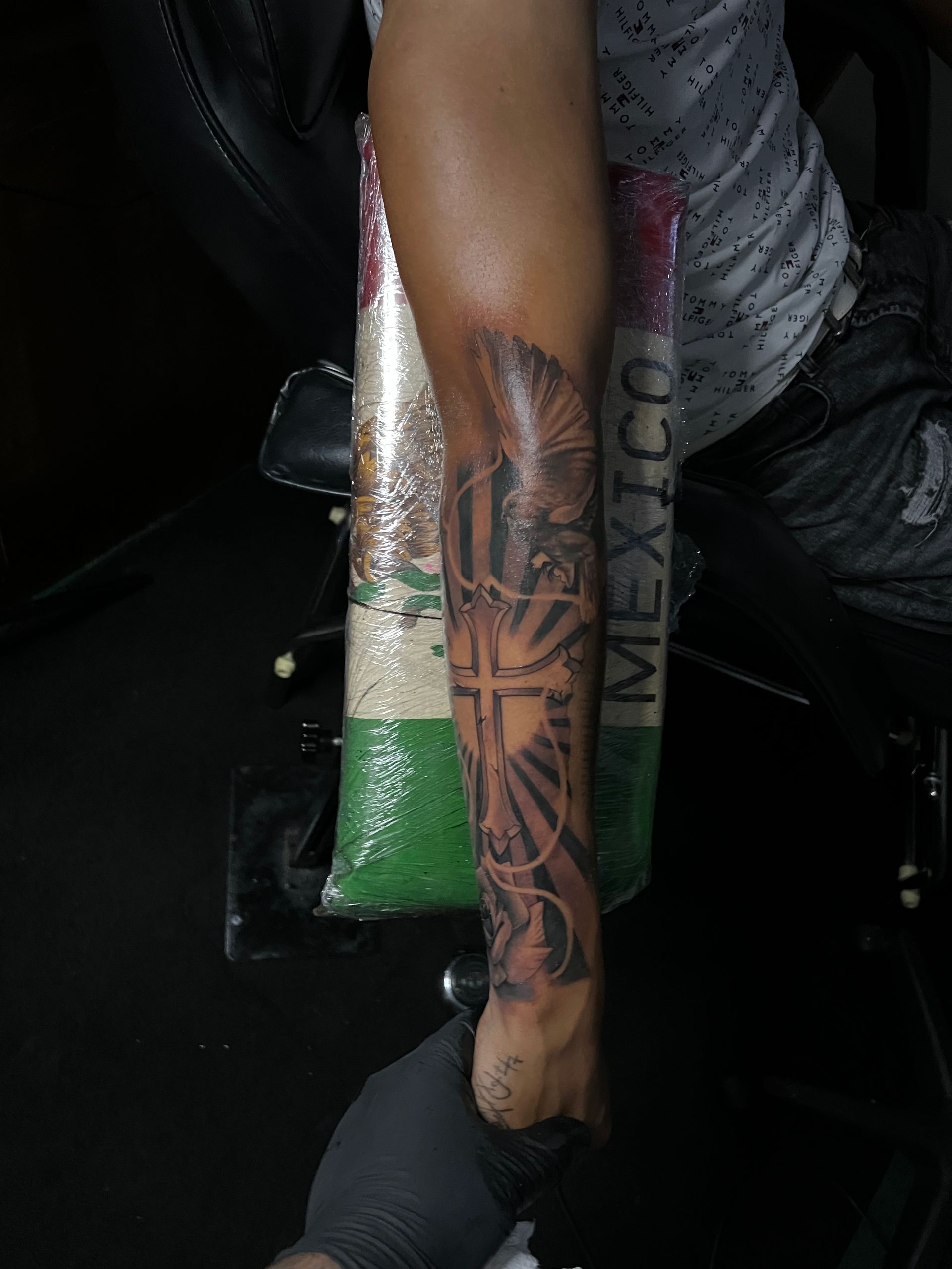 Tattooed arm with a cross, rays, and other designs, likely religious, in a tattoo shop.