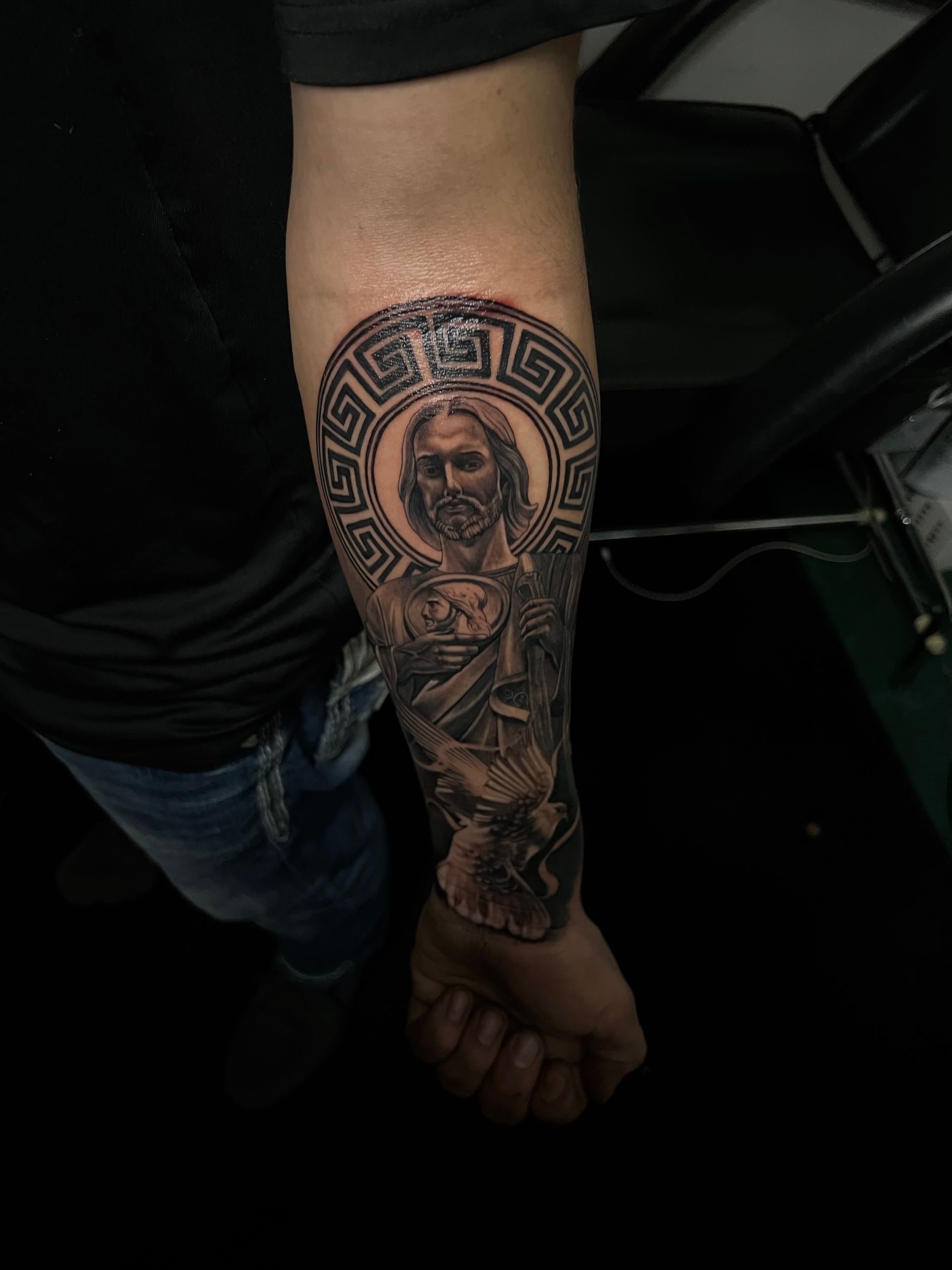 Detailed arm tattoo of a figure in a halo, surrounded by a Greek key design, extending down the arm.