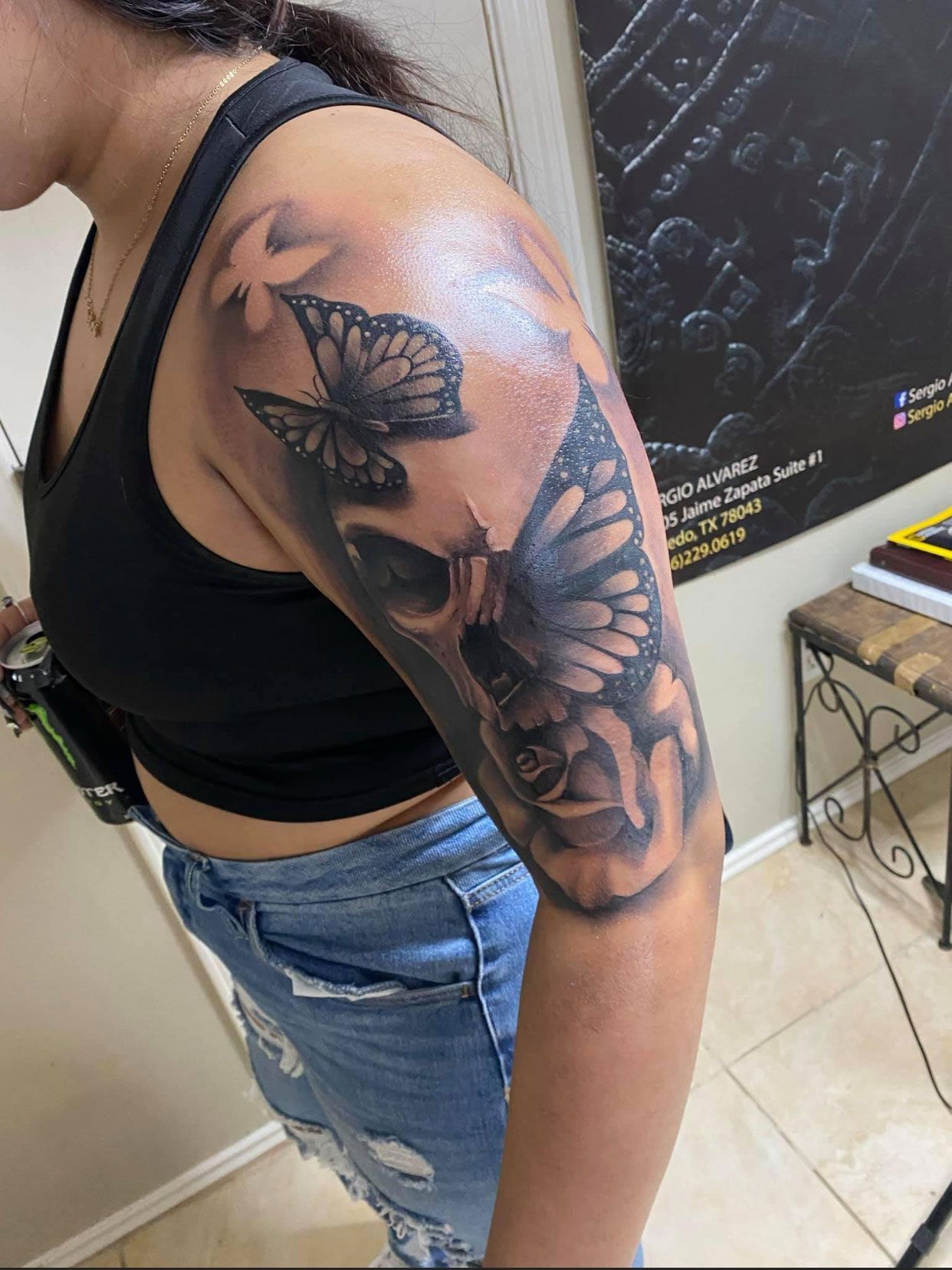 Woman's arm tattoo: skull, butterflies, and a rose in black and gray ink.