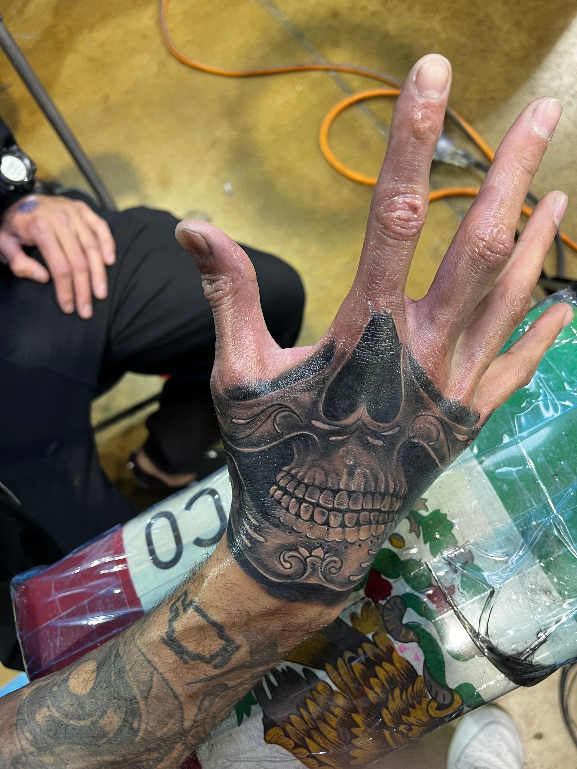 Hand tattoo of a detailed skull. Hand raised with fingers spread. Black and gray ink.