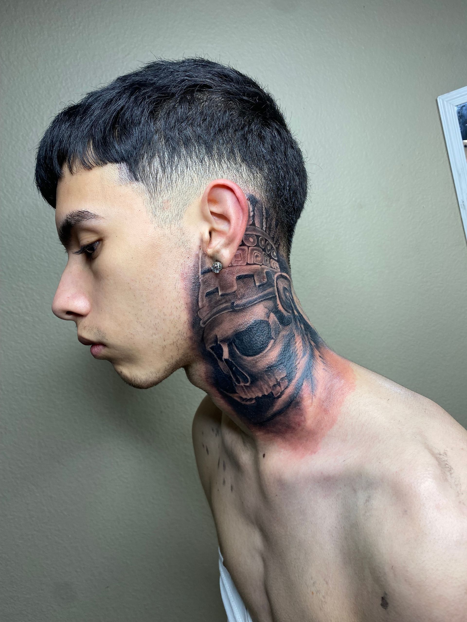 A young man with a neck tattoo, red skin irritation. He has a faded haircut and is turned to the side.