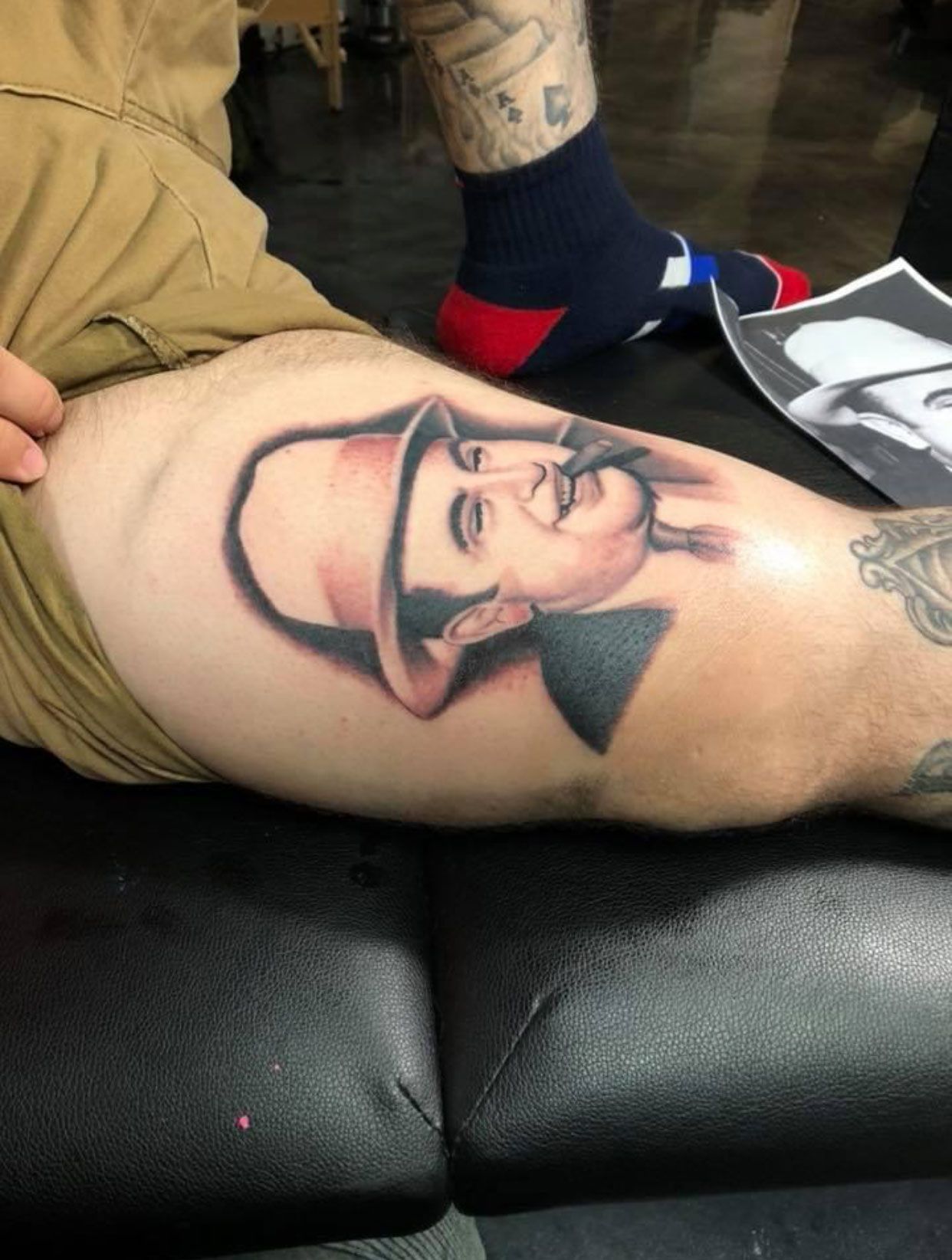 Tattoo of a man in a top hat and bow tie, smoking a cigar, on a person's leg.