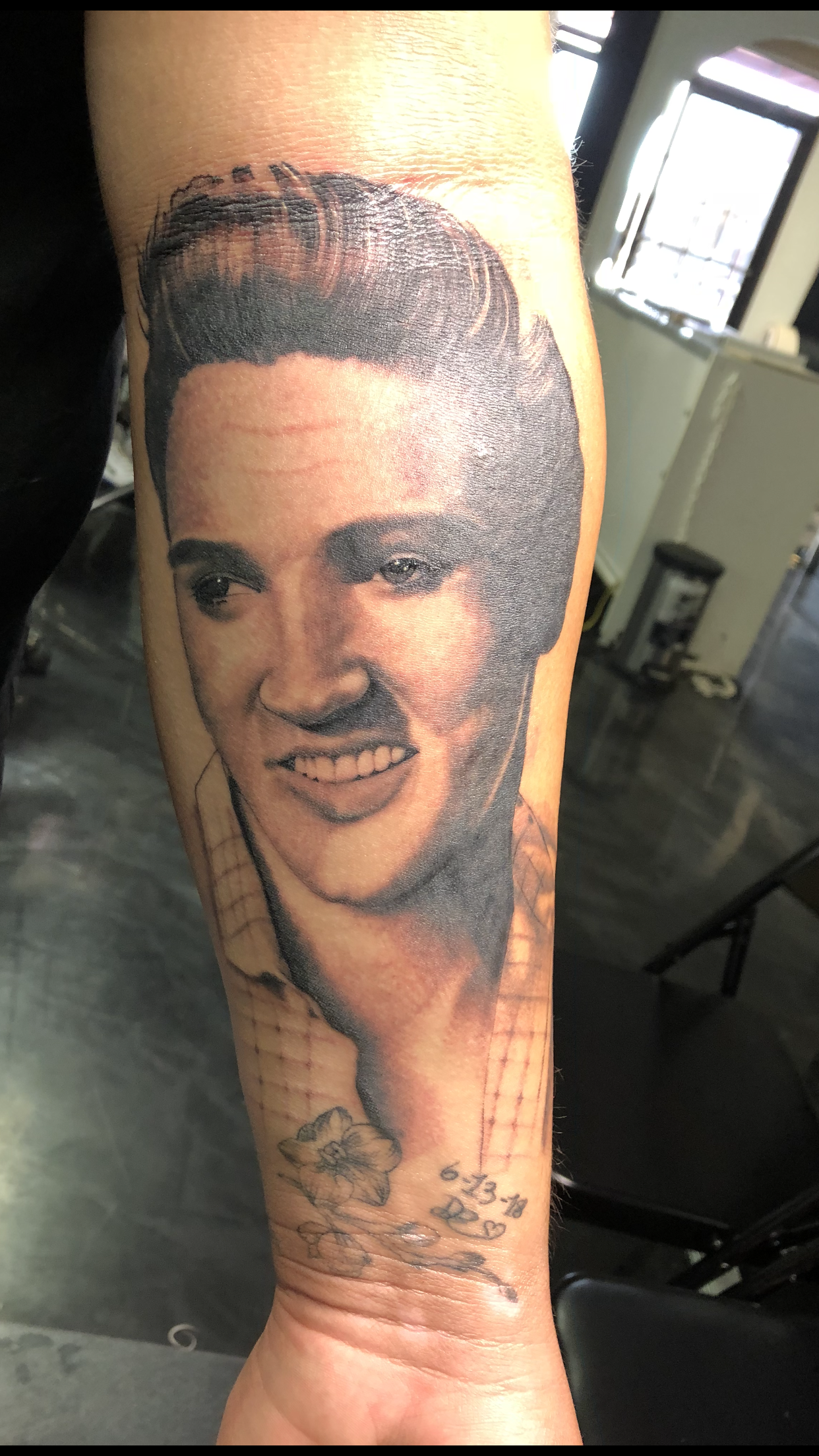 Tattoo of Elvis Presley on an arm, black and white, smiling, with a pompadour hairstyle.