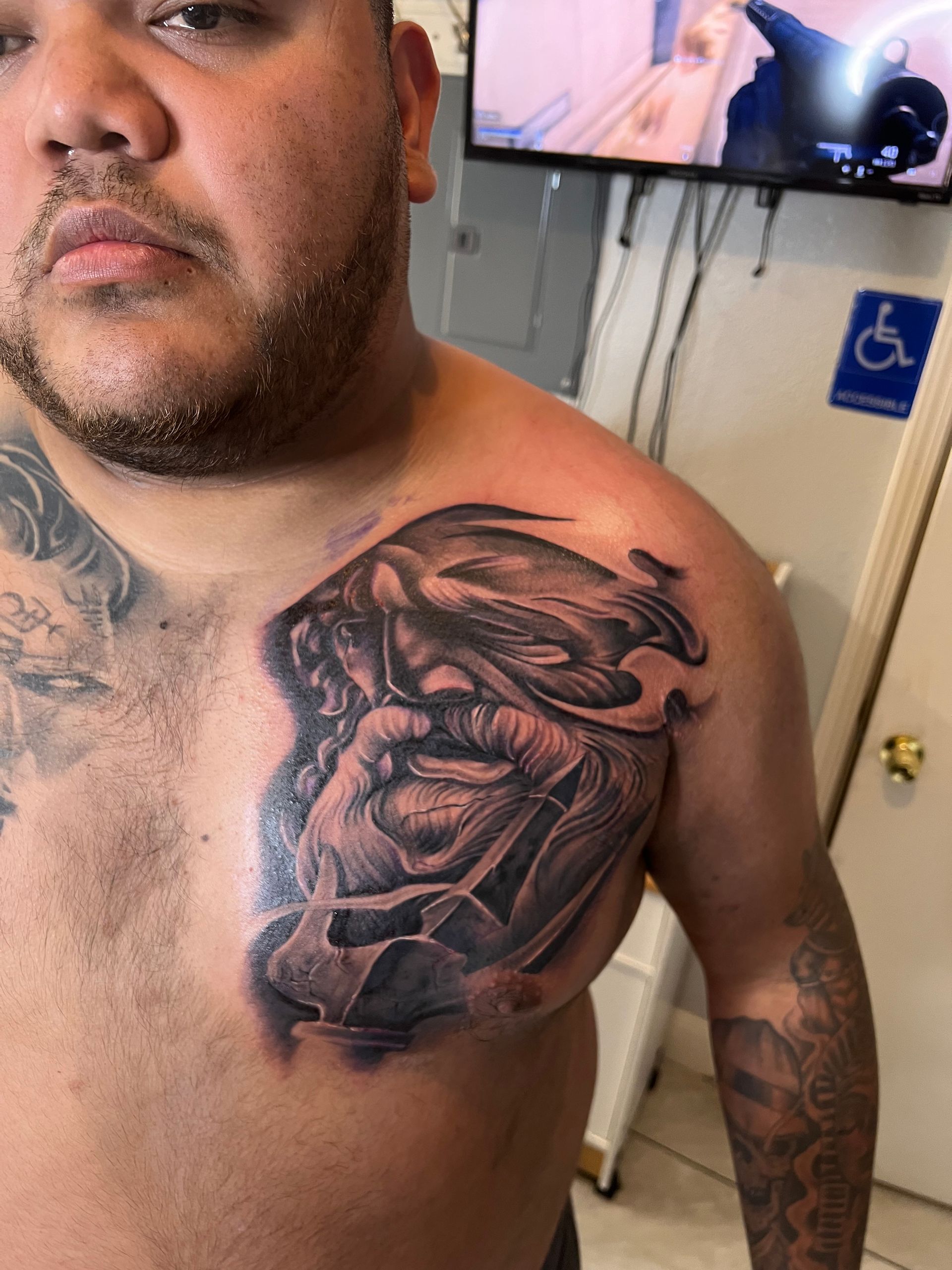 Man with chest tattoo of a bearded figure, in a tattoo shop.