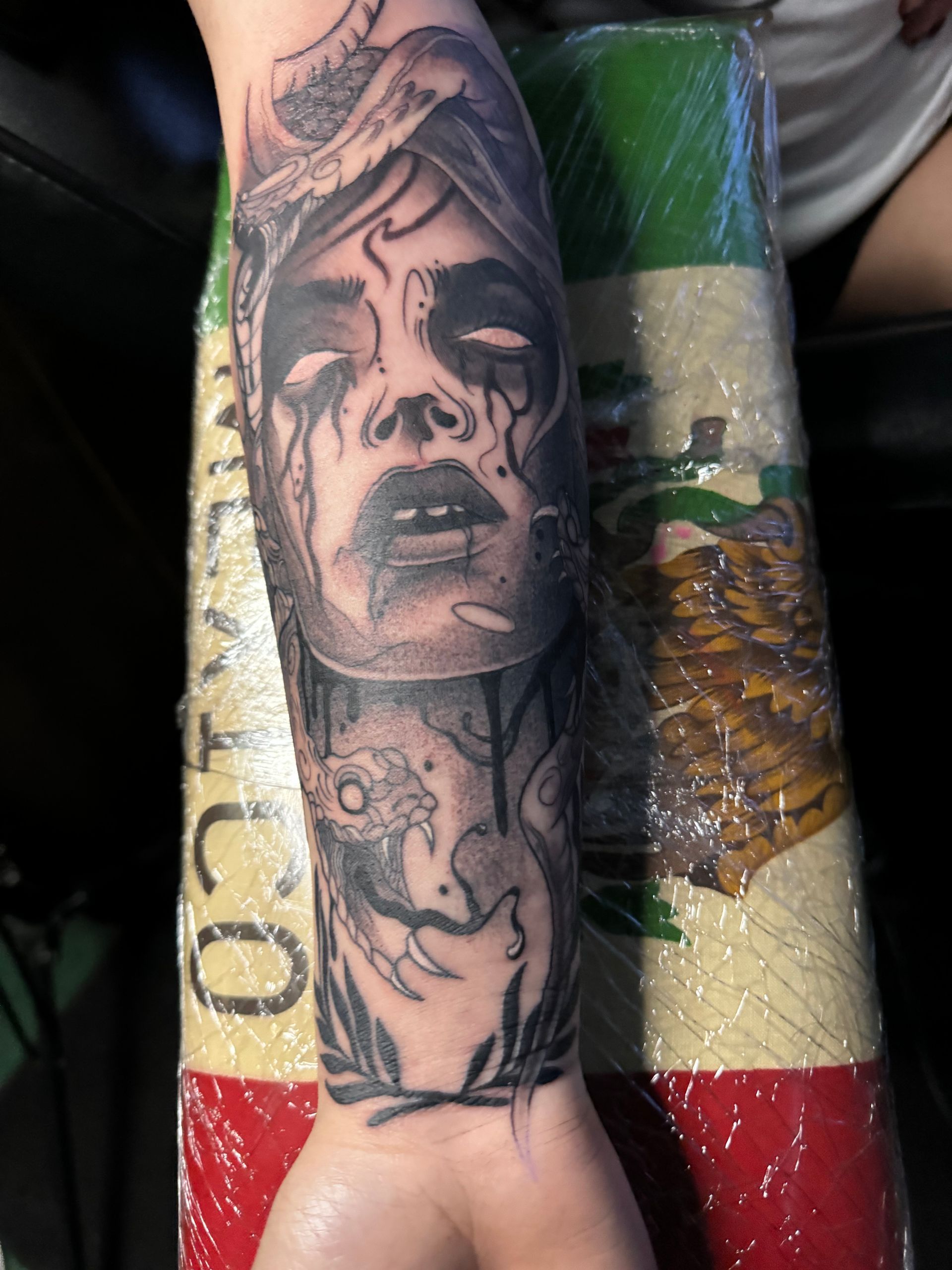 Tattoo of a Medusa-like woman with tears on forearm, black and gray ink.