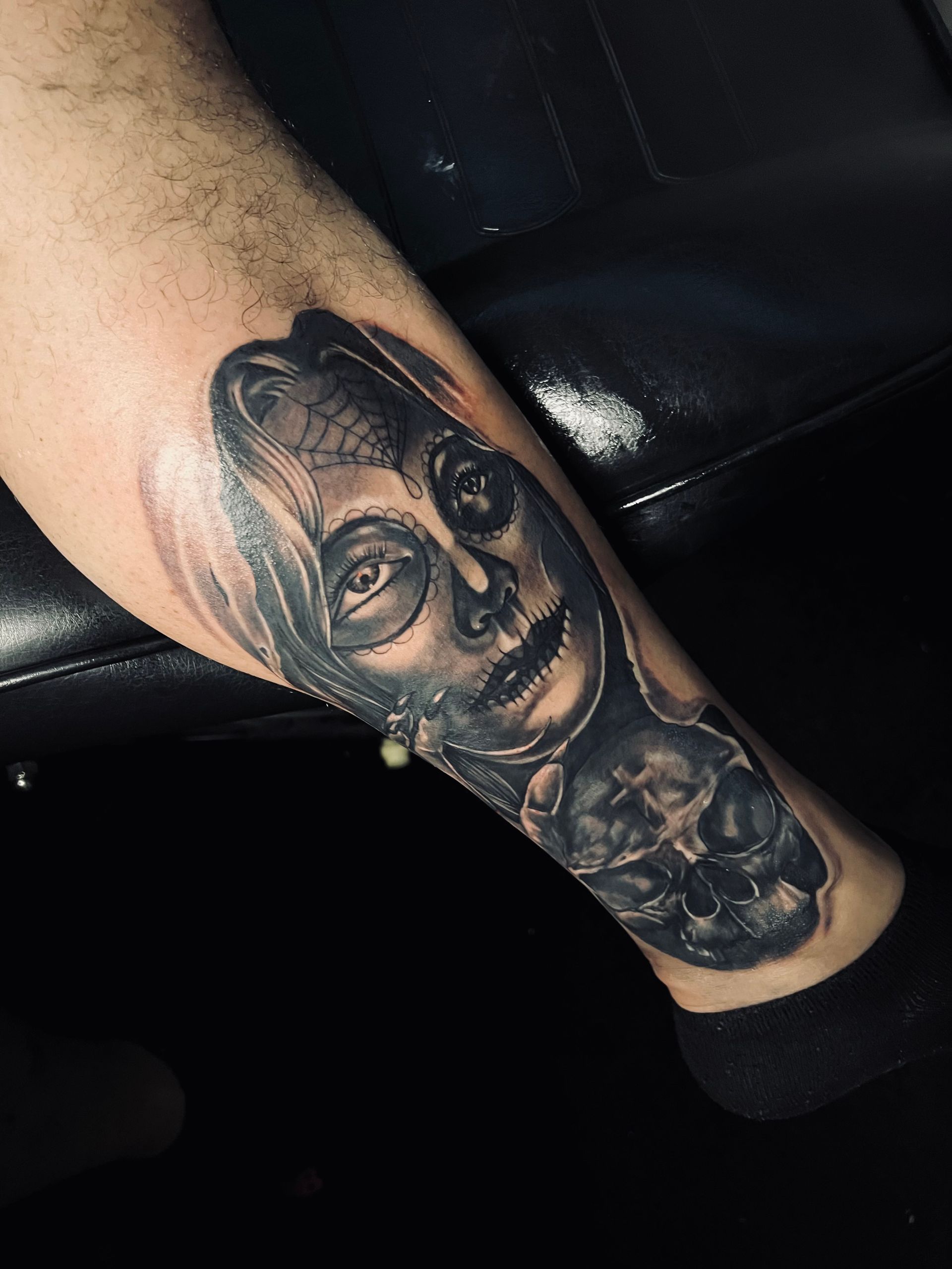 Black and gray tattoo of a woman's face on a leg, with a skull-like appearance, detailed shading.