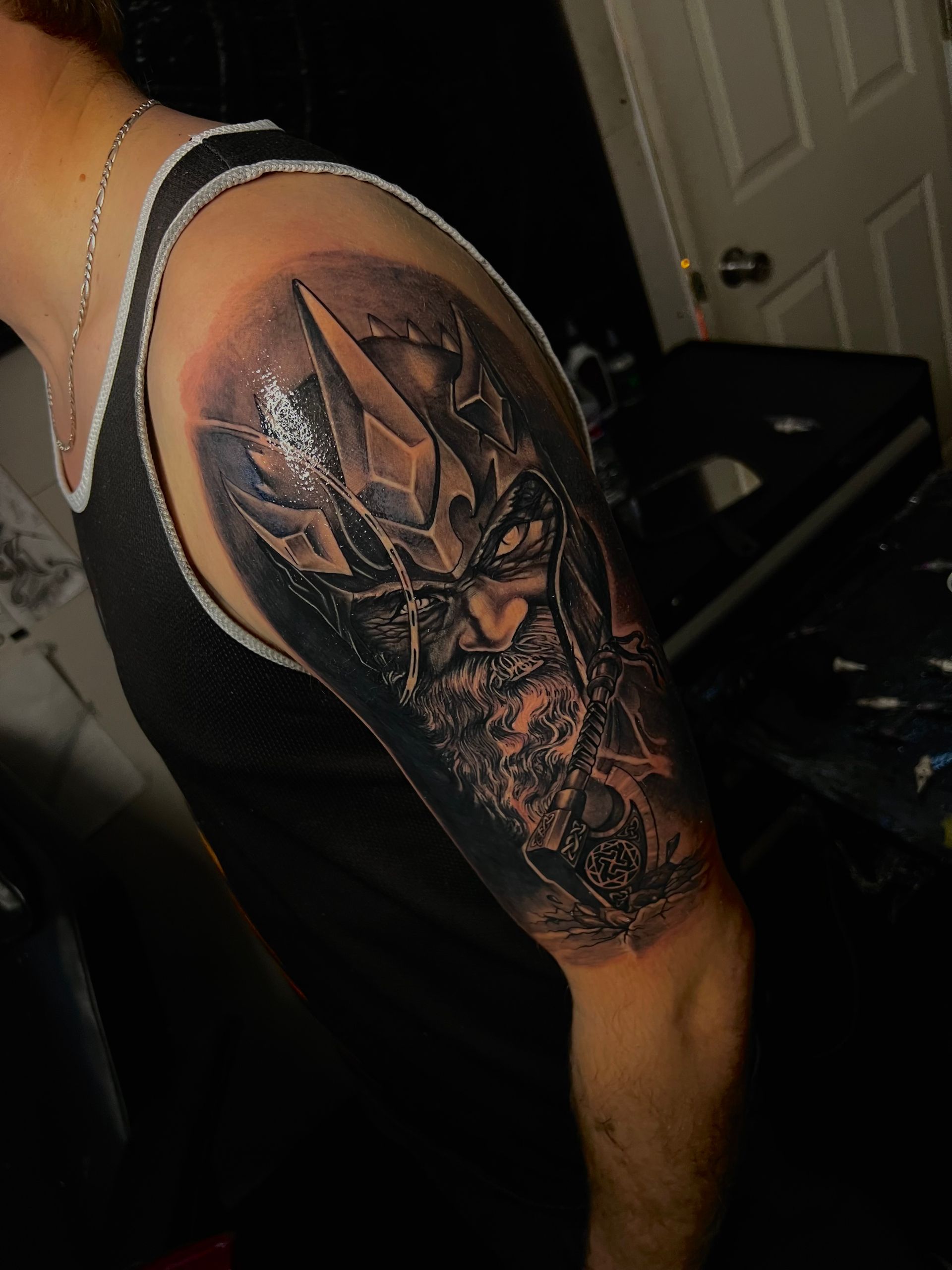 Black and gray shoulder tattoo of a bearded king wearing a crown, with dark shading around him.