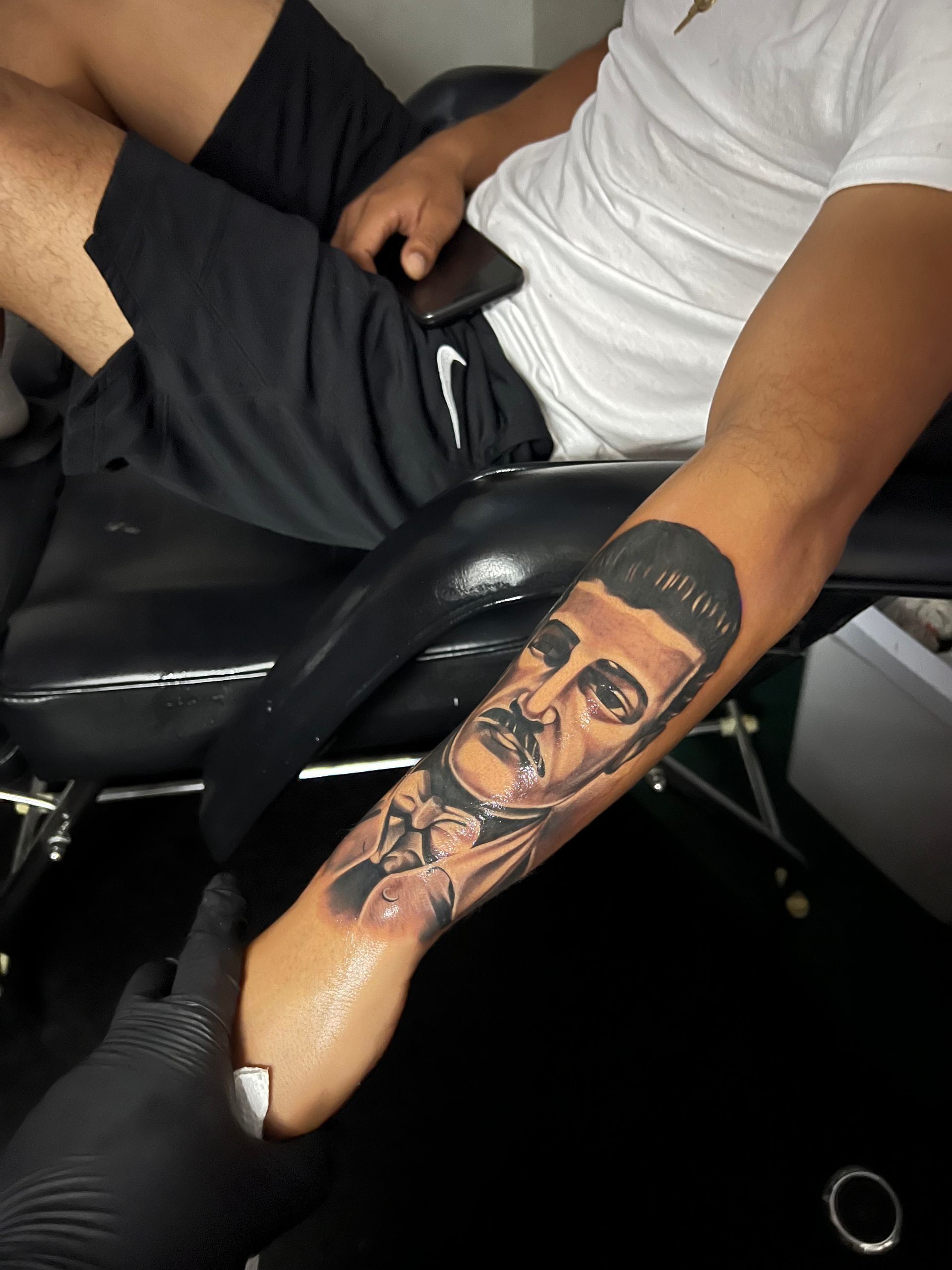 Tattoo of a man's face on a forearm; the artist is working on the tattoo.