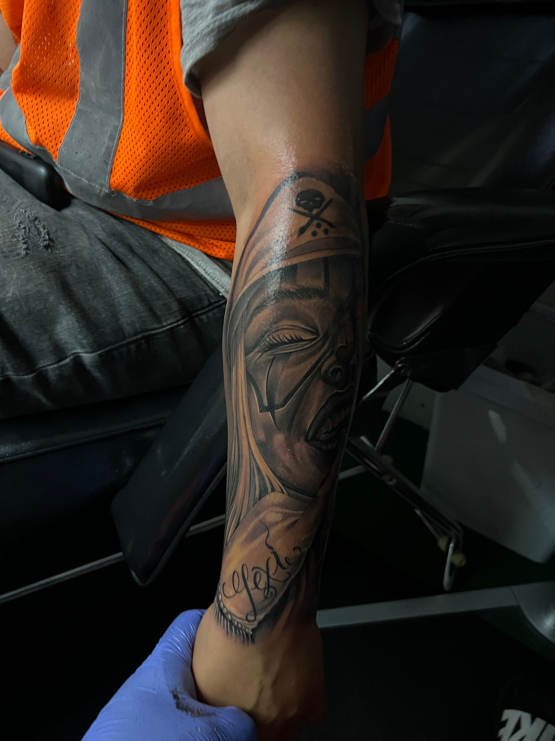 Person with a forearm tattoo; a religious figure's face; wearing an orange safety vest.
