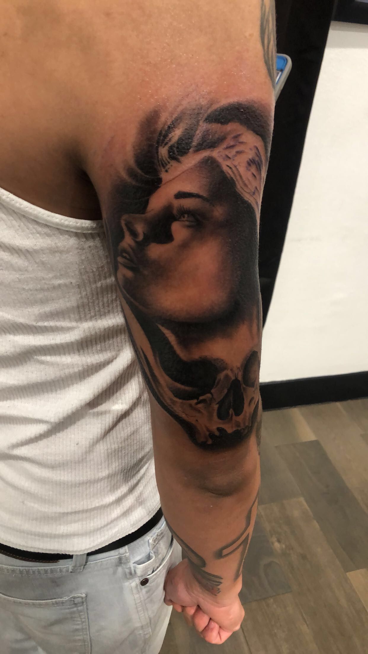 Arm tattoo featuring a woman's face fading into a skull; gray-scale with shading.