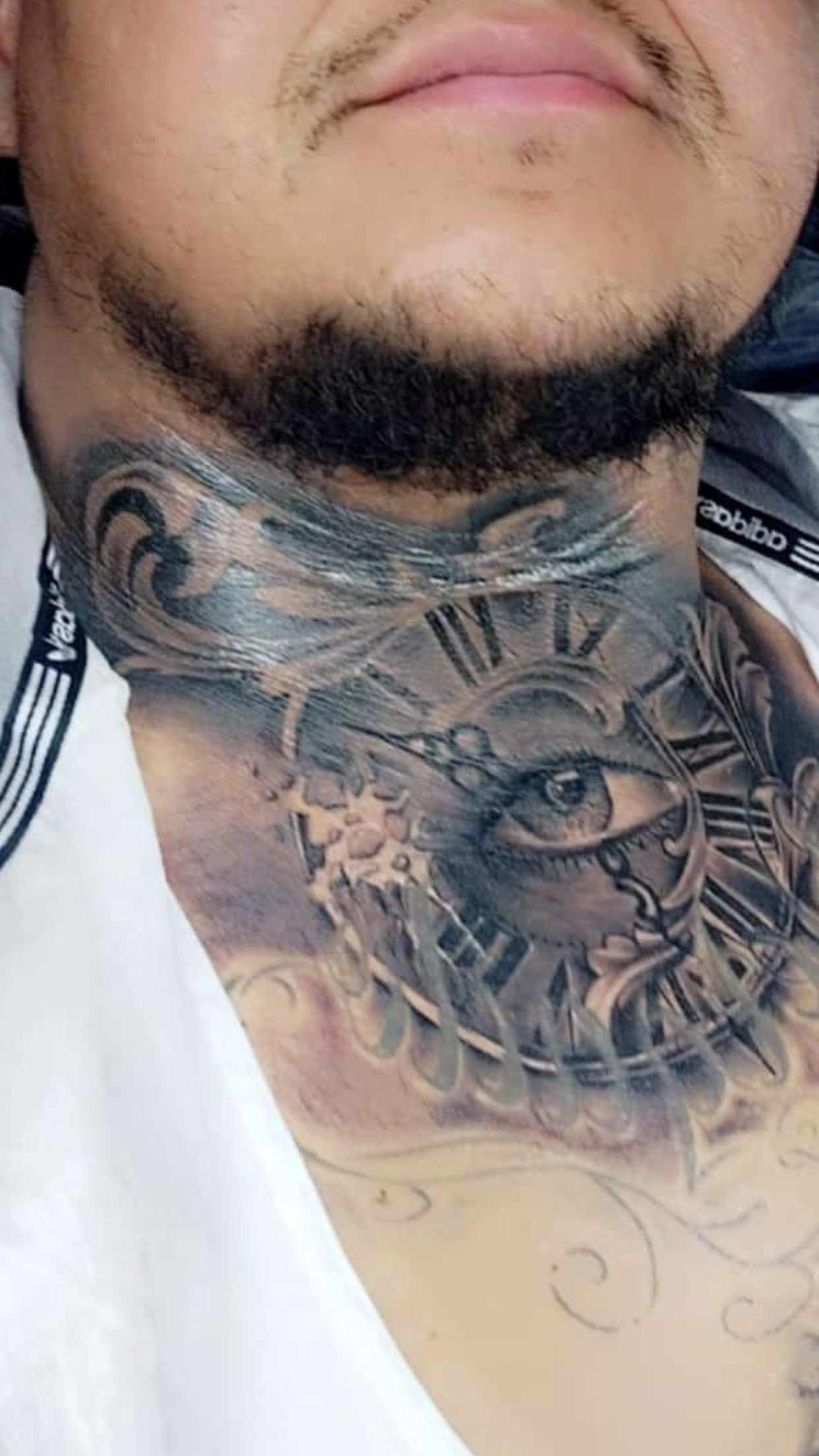 Man's neck tattoo: clock with eye, gray shading. He wears a white collared shirt, close up of face.