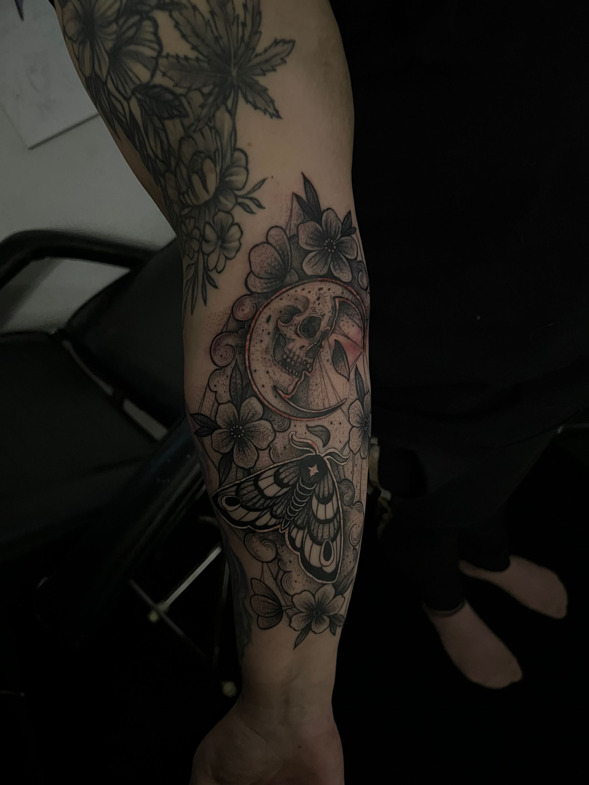 Tattoo of a demonic mask with cherry blossoms on a person's arm; black and white design.