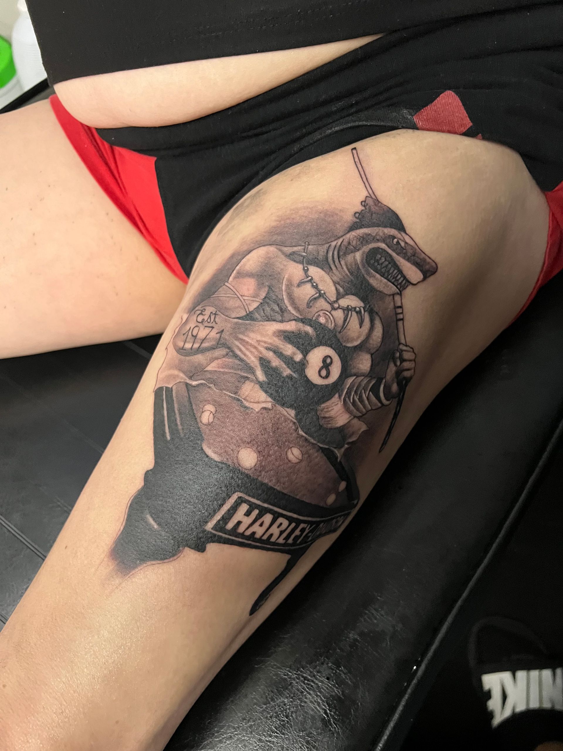 Tattoo on thigh: a muscular turtle playing pool, holding an 8-ball and cue. Name on the base: