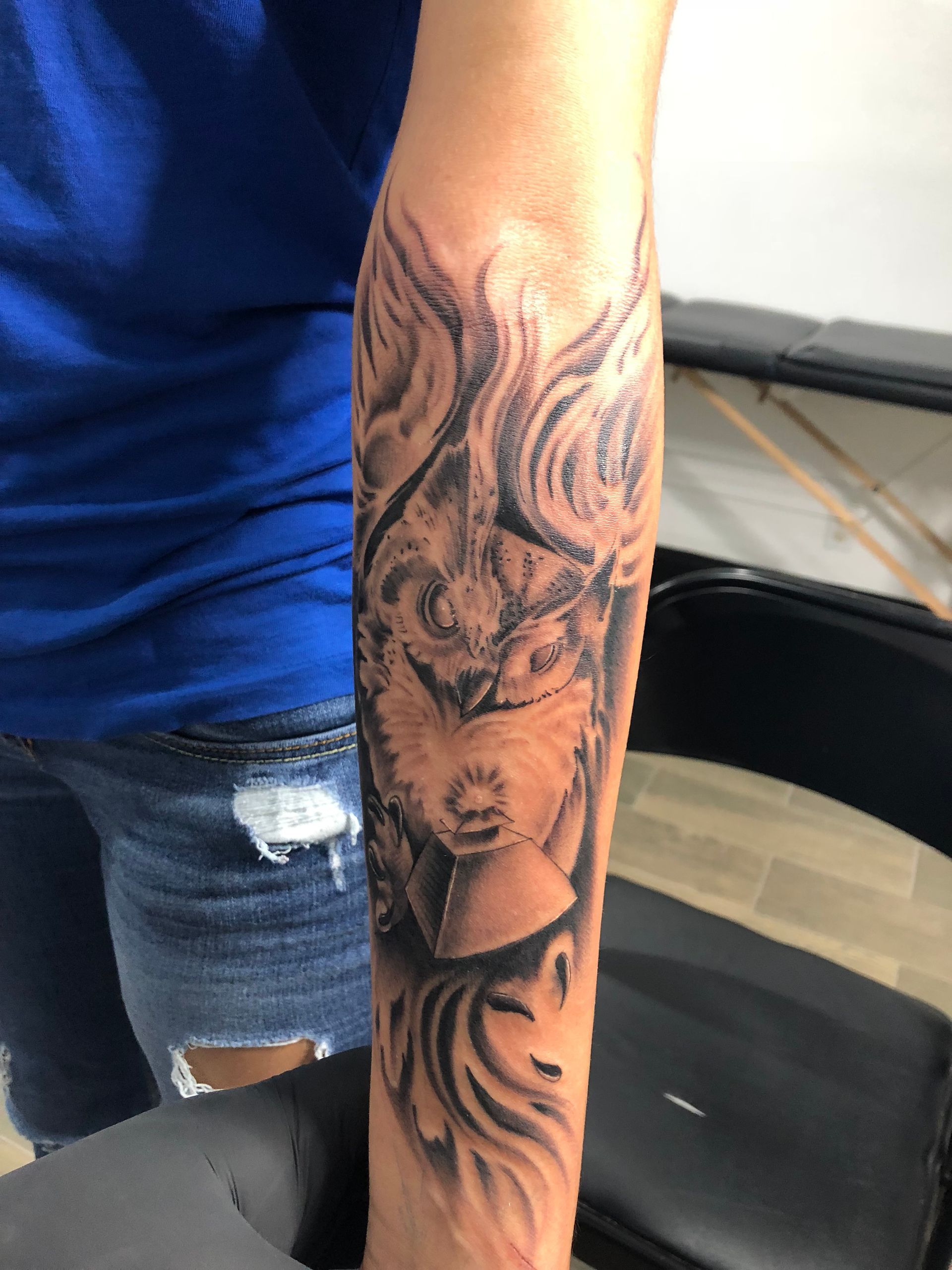 Tattoo of a wolf's face on a forearm, surrounded by flame-like shading; grayscale.