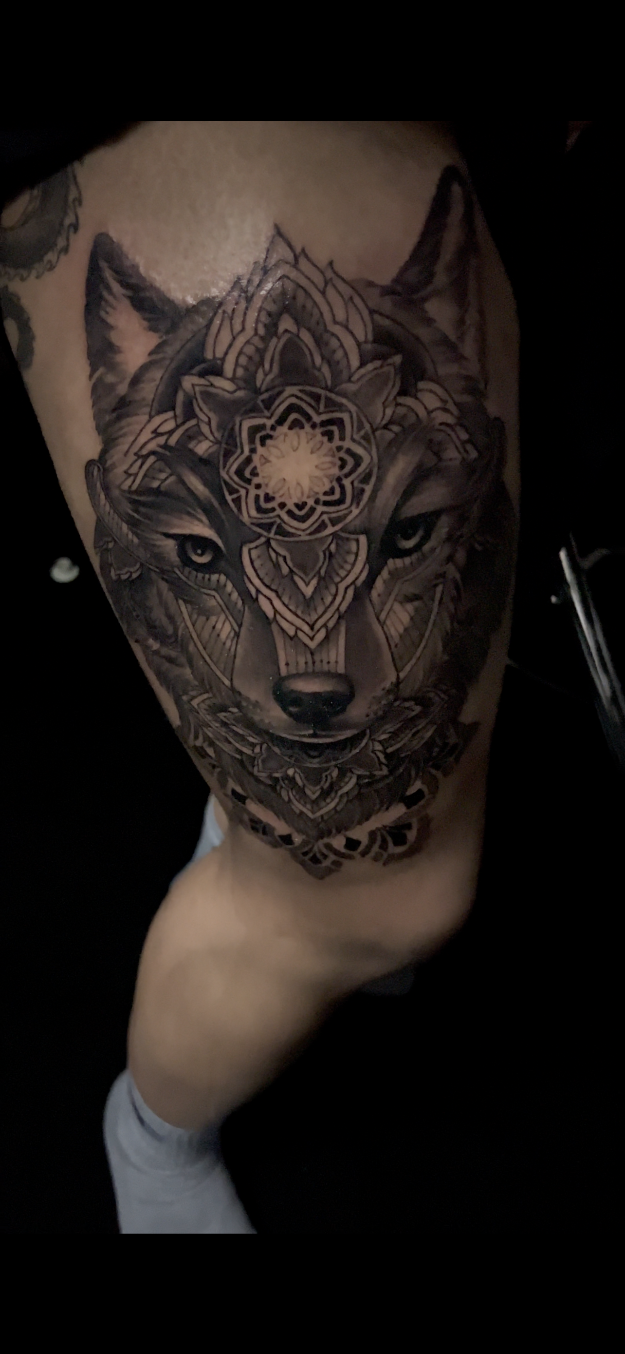 Wolf tattoo on a leg, intricate geometric designs overlay the wolf's face, black and gray.
