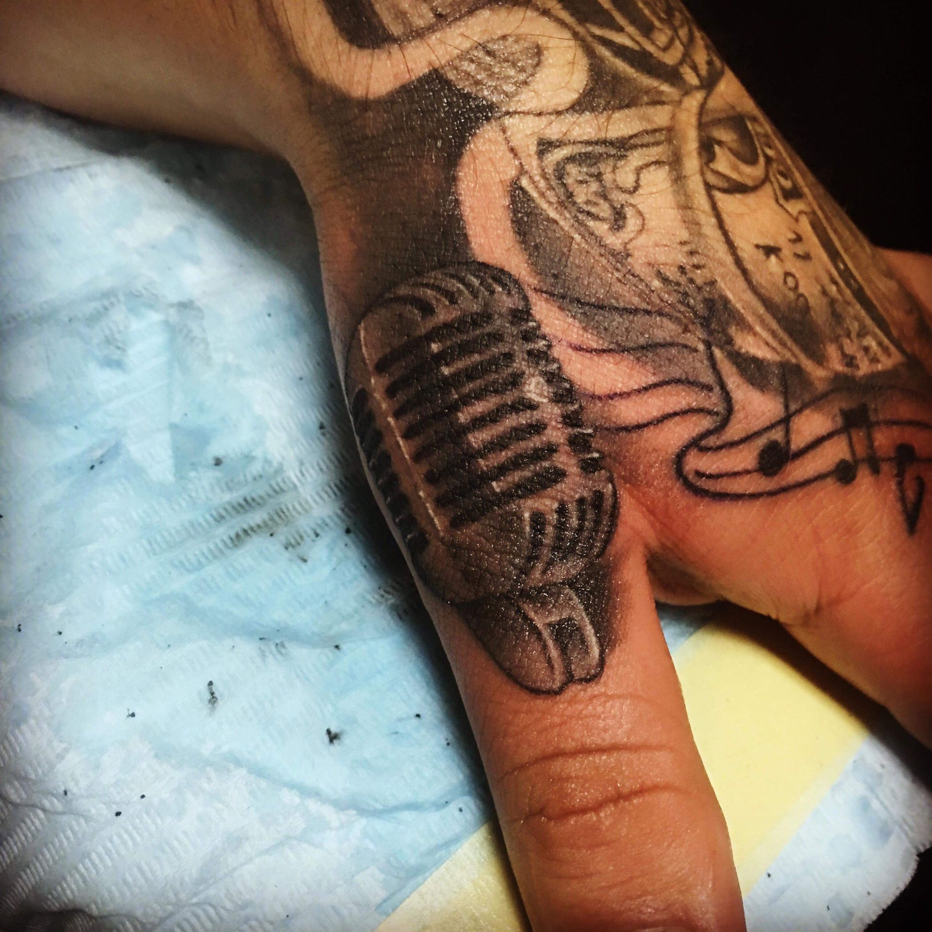 Tattoo of a vintage microphone on a thumb; other tattoos visible on the hand.