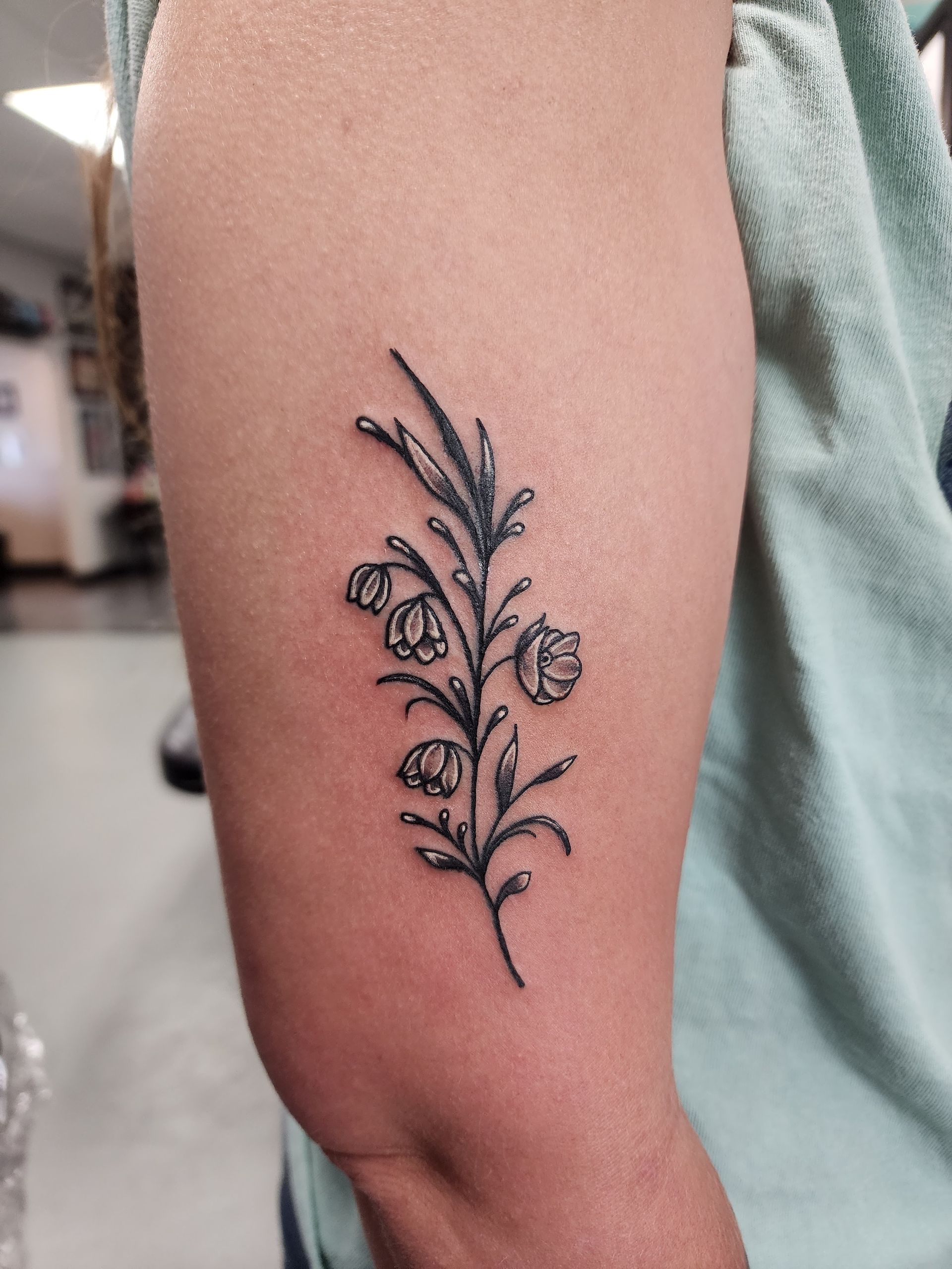 Black and white floral tattoo on a person's upper arm, with delicate line work.