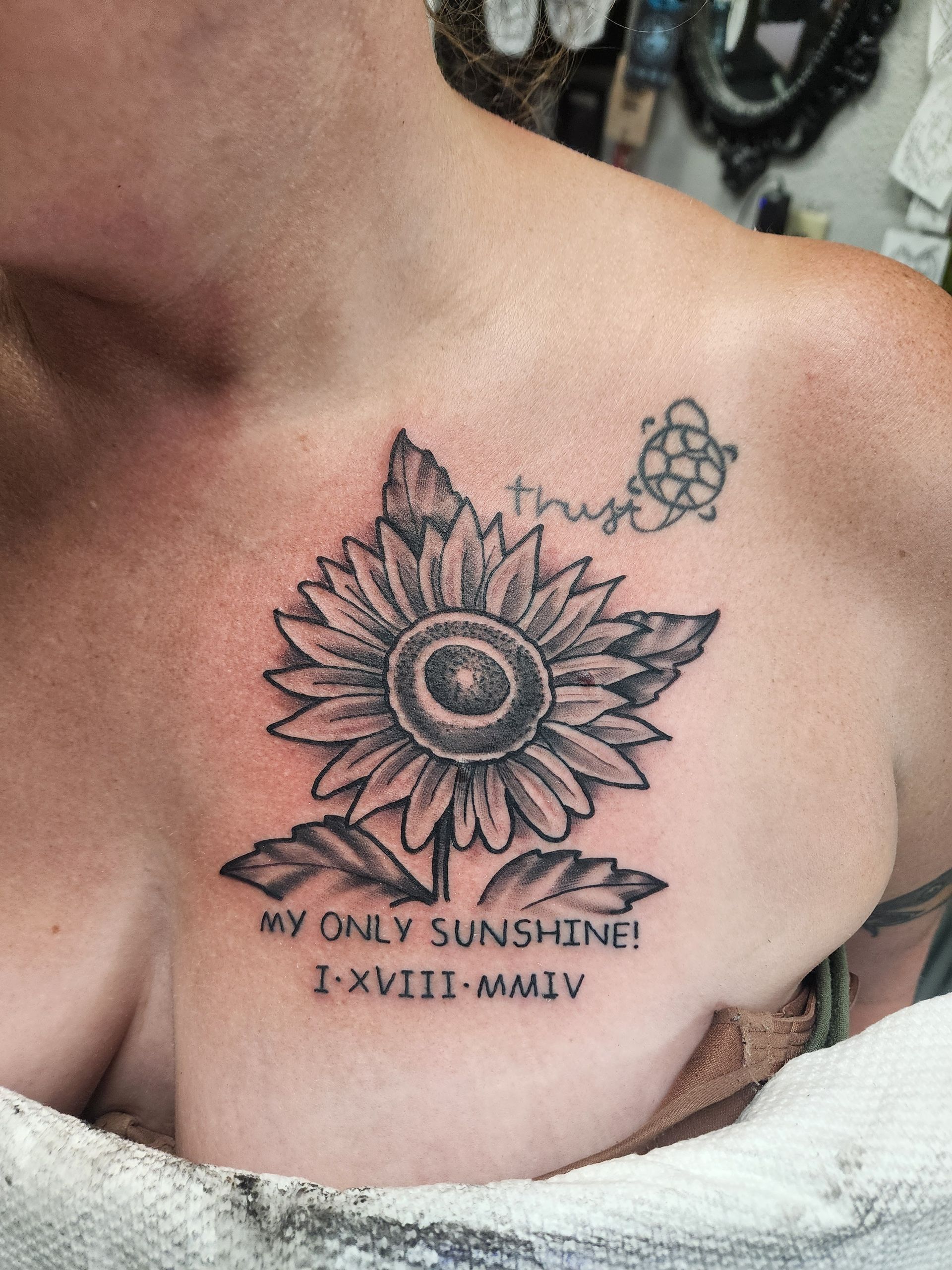 Tattoo of a sunflower on a person's chest, with the words 