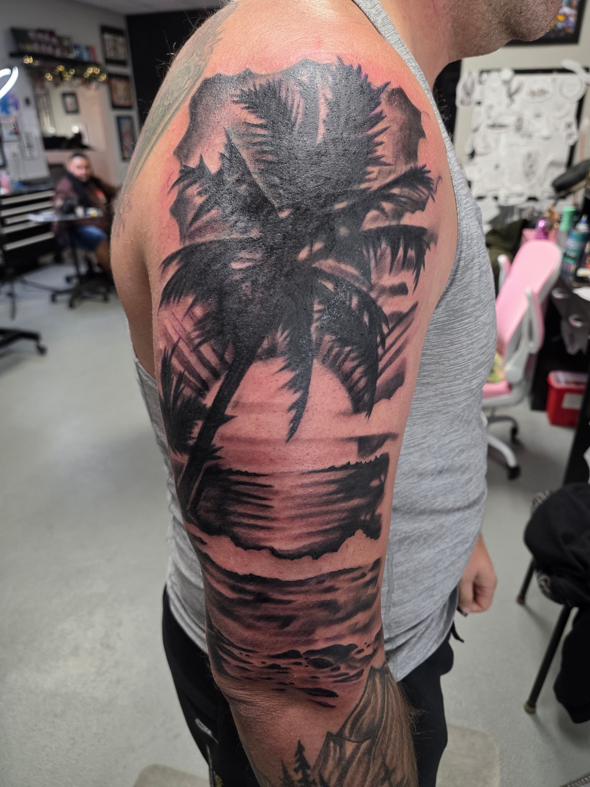 Tattoo of a black palm tree and ocean scene on a man's arm.  Studio setting.
