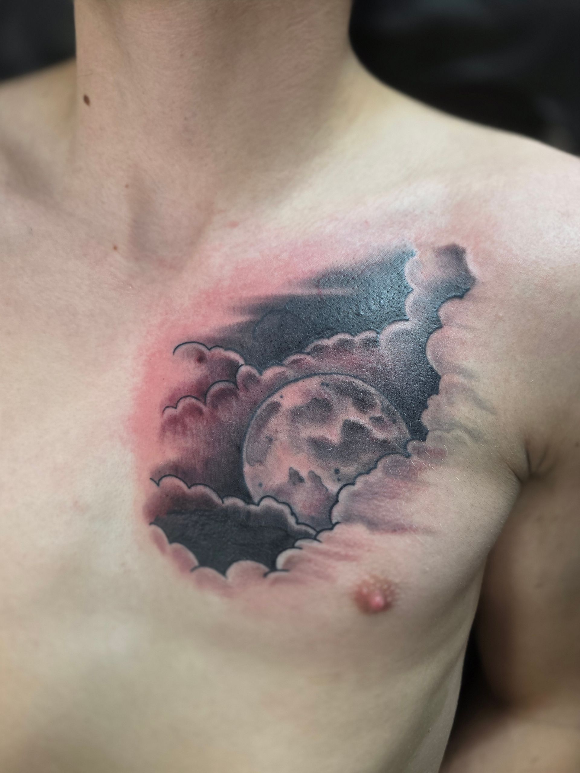 Chest tattoo: Moon peeking through dark clouds, set against a red, irritated skin.