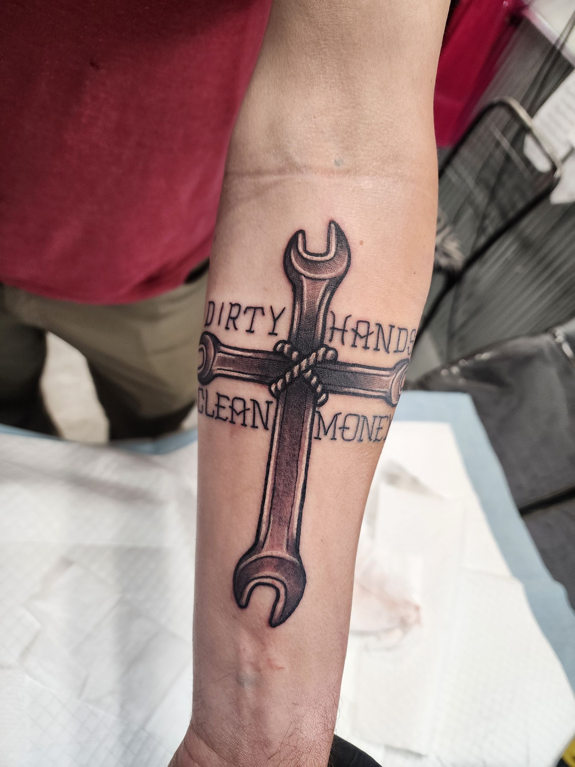 Tattoo on forearm: wrench cross with text 