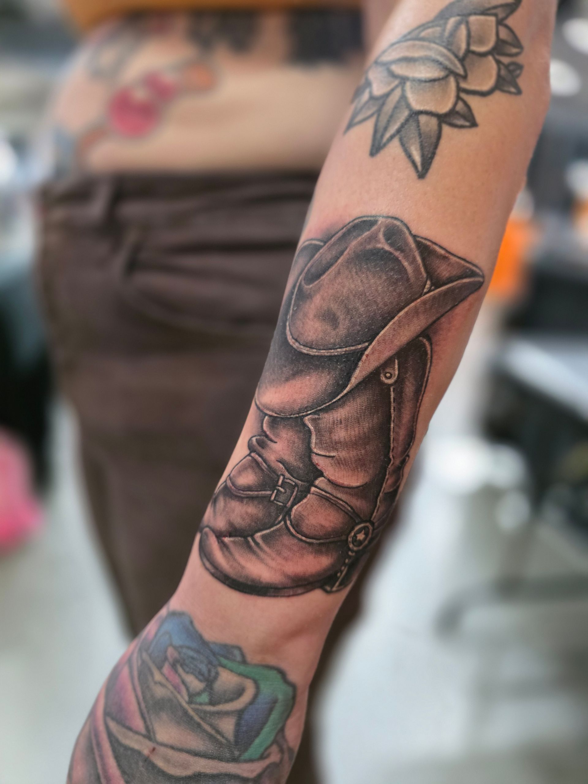 Black and white cowboy boot tattoo on a person's forearm, with other tattoos visible.