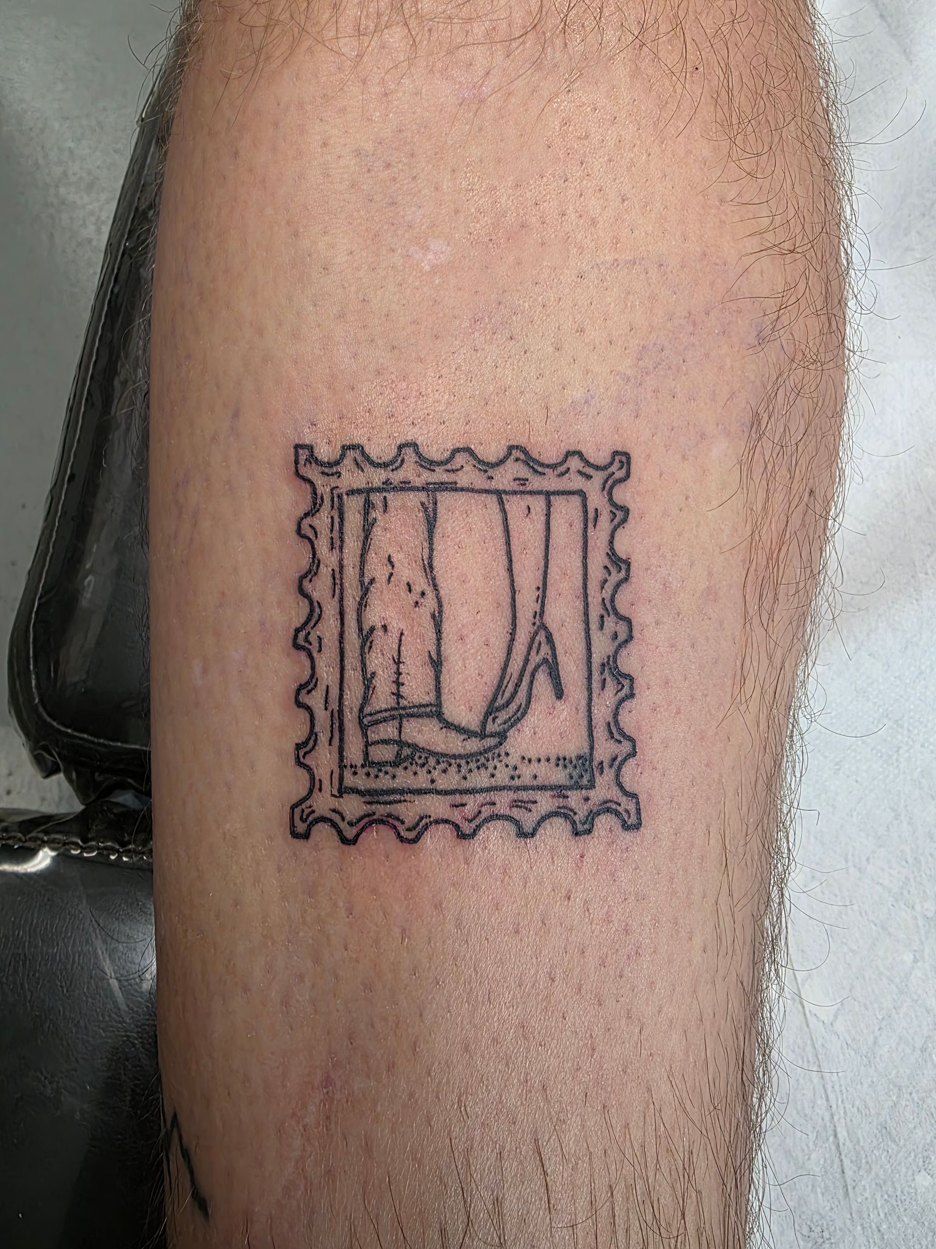 Tattoo of a postage stamp on an arm, showing legs and a high heel shoe.