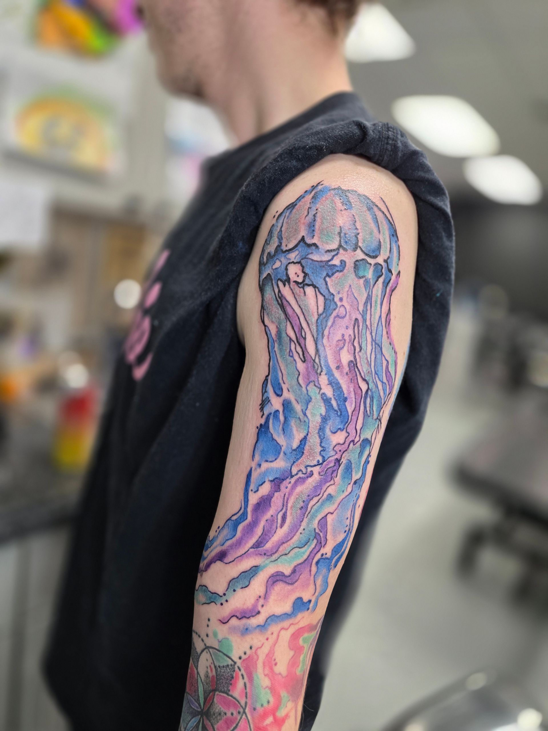 Person with a blue and purple jellyfish arm tattoo, standing indoors.