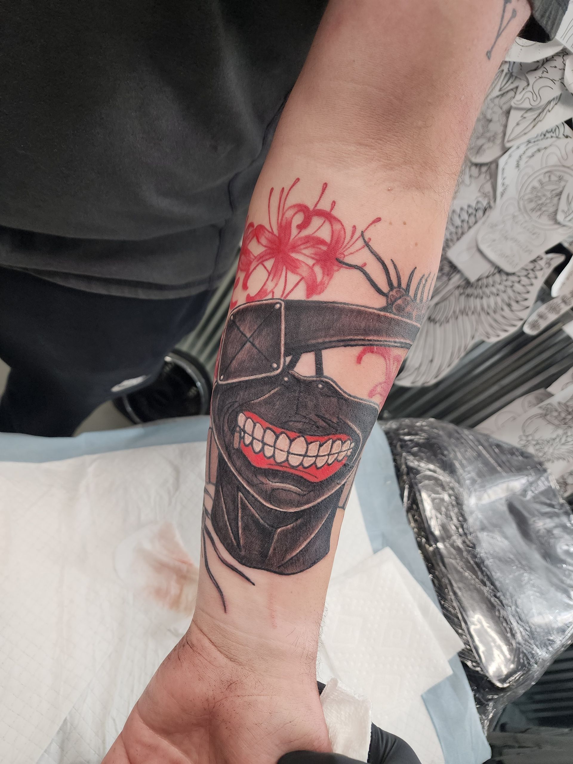 Tattoo of a black mask with red flowers on a person's forearm, in a tattoo studio.