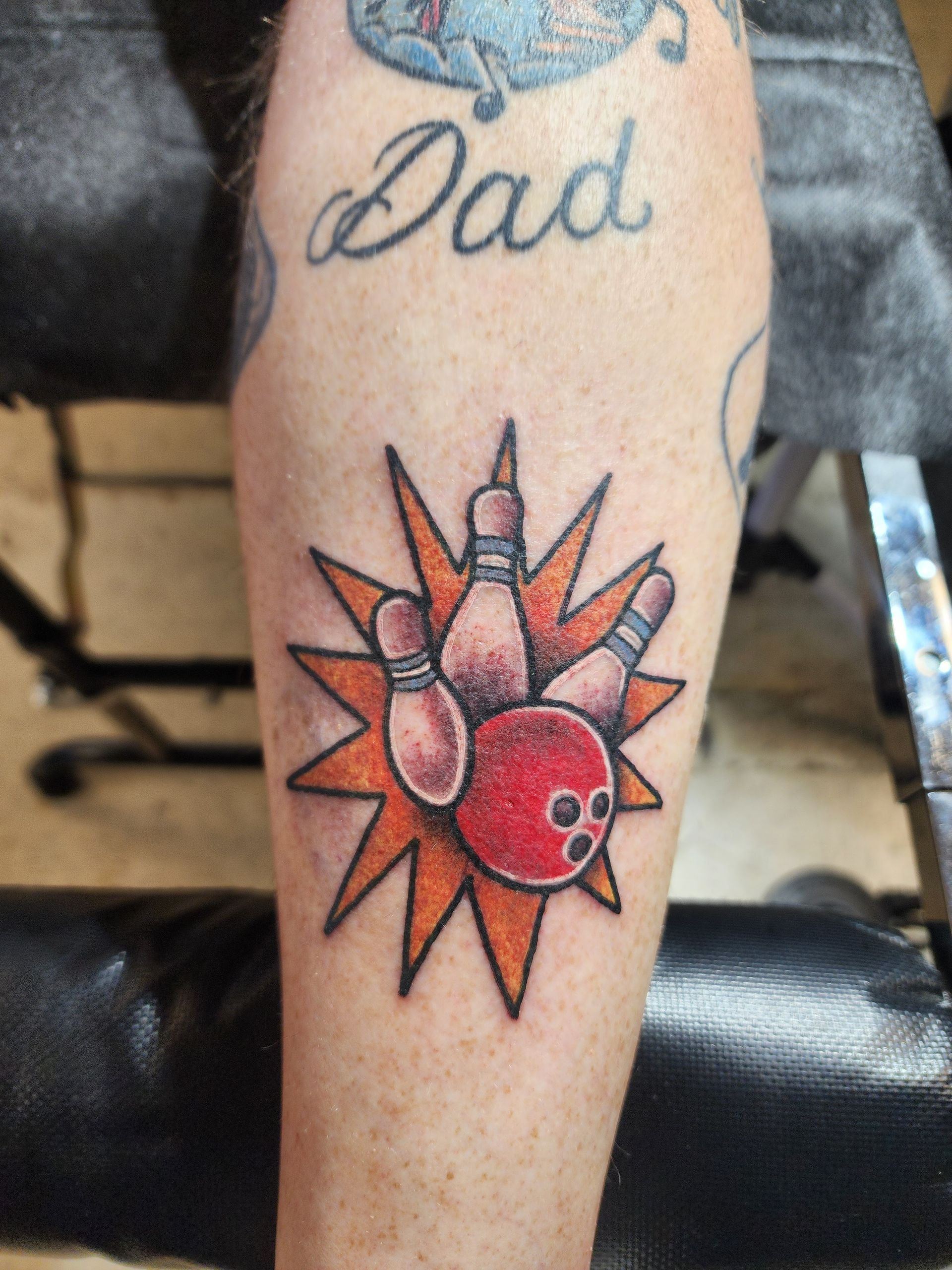 Bowling strike tattoo with orange starburst on a leg; 
