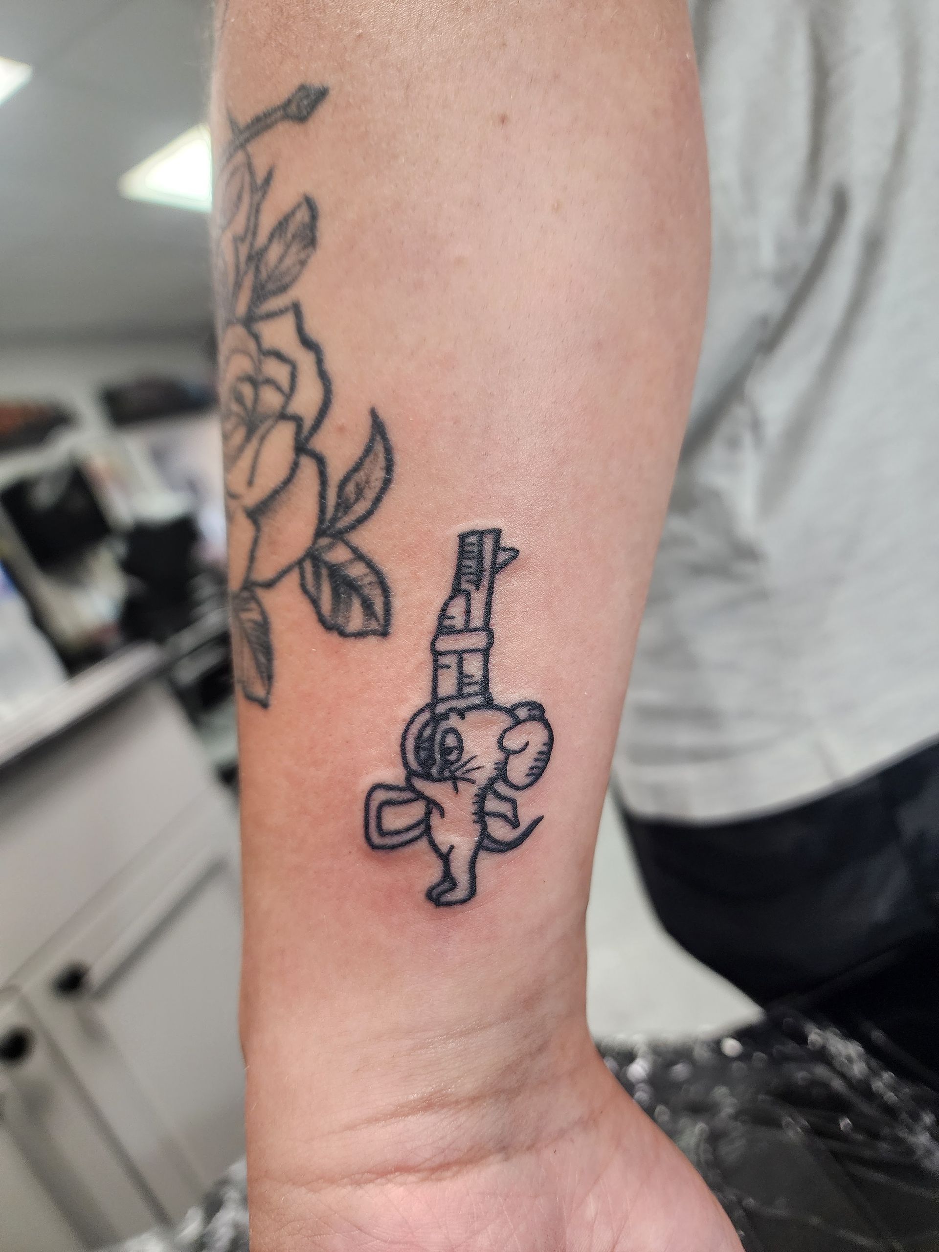 Tattoo of a stylized elephant holding a gun, on a person's wrist. A rose tattoo is also visible.