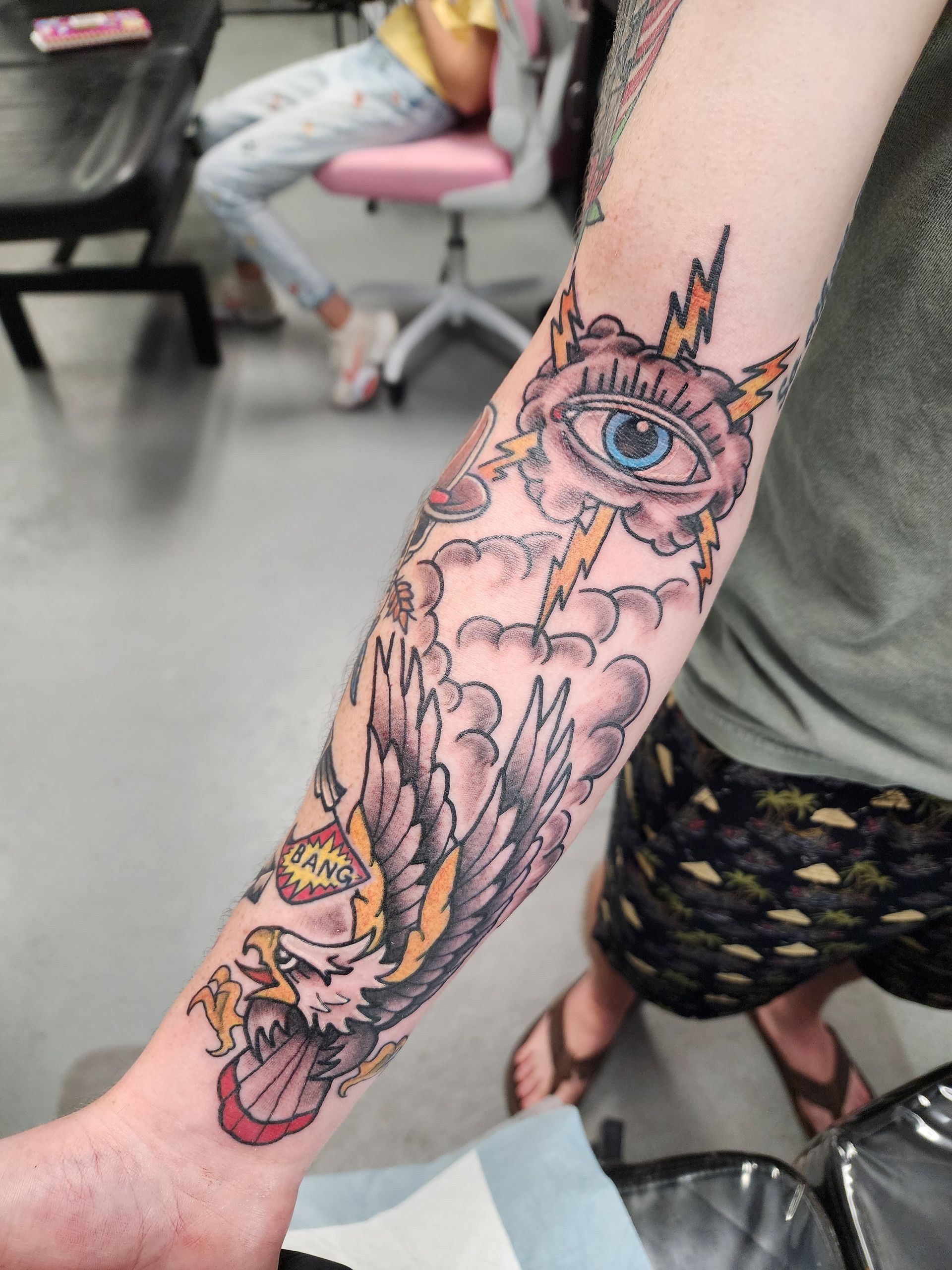 Tattoo of an eye, lightning, clouds, and an eagle on a forearm.