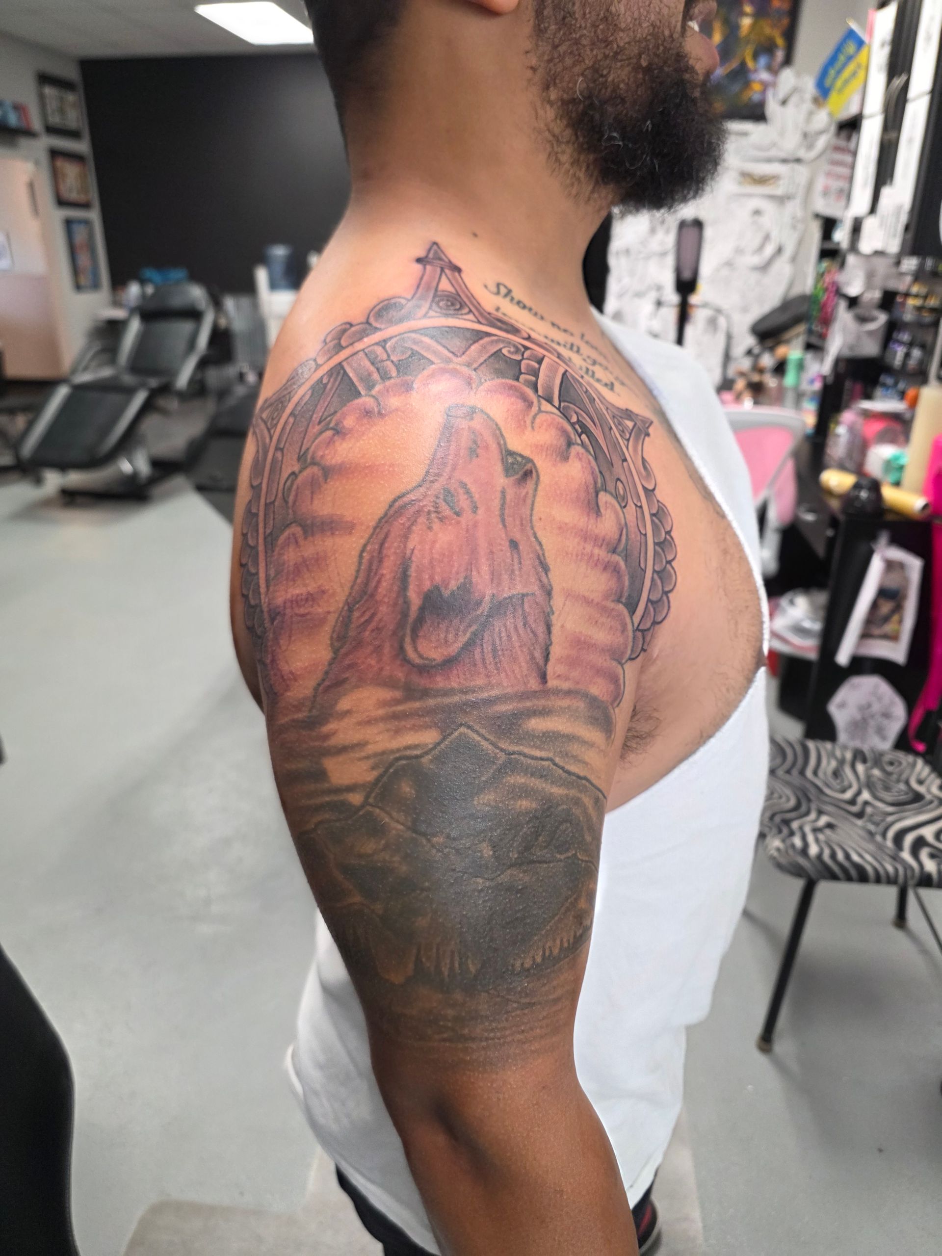 Tattoo of a figure in an ornate arch on a man's upper arm. The setting is a tattoo shop.