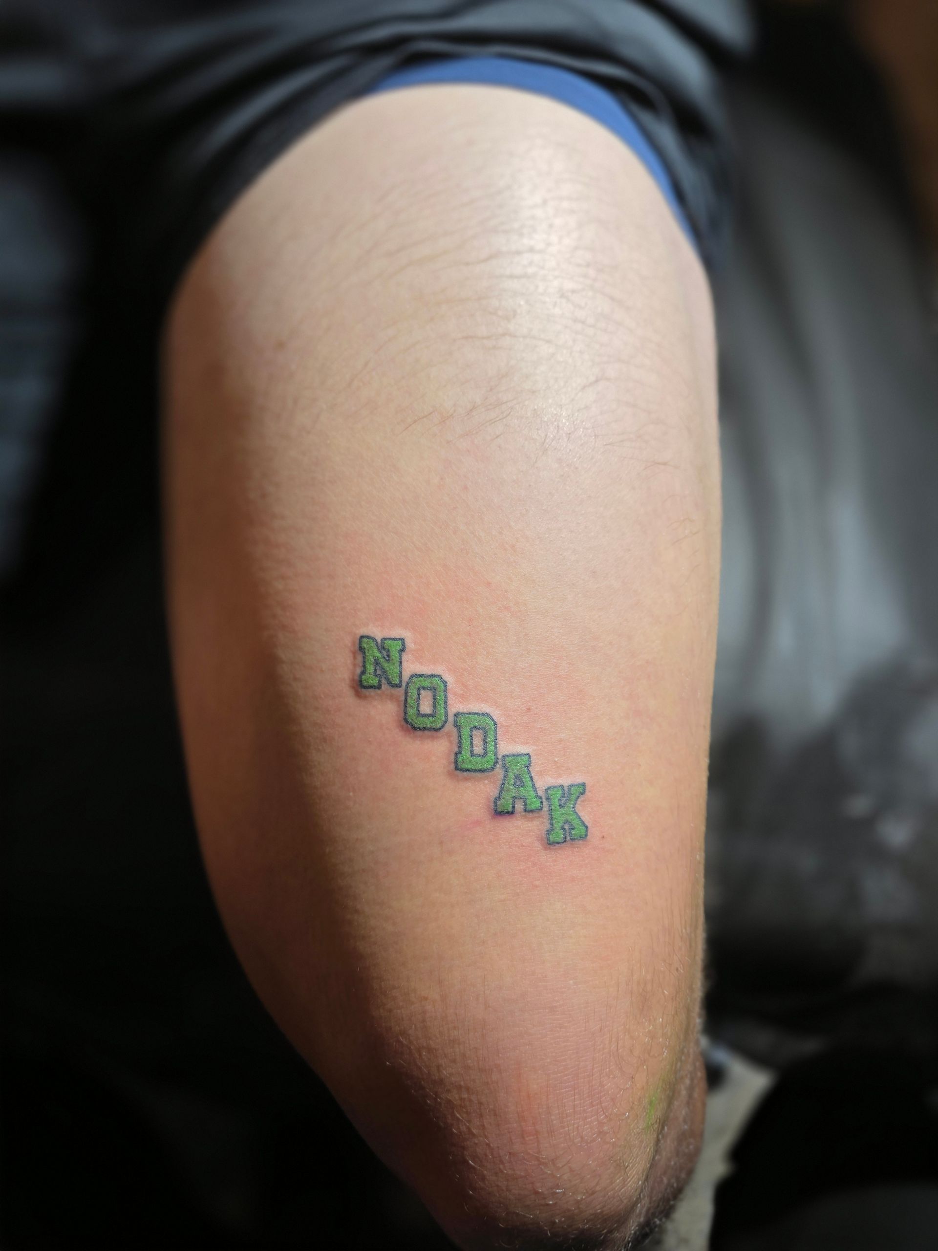 Green-ink tattoo of the word 