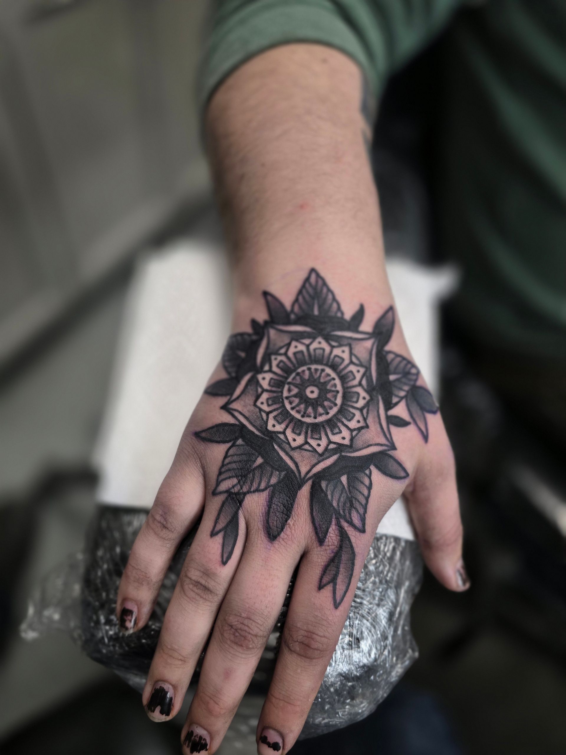 Hand tattoo: black and white mandala with surrounding leaves.