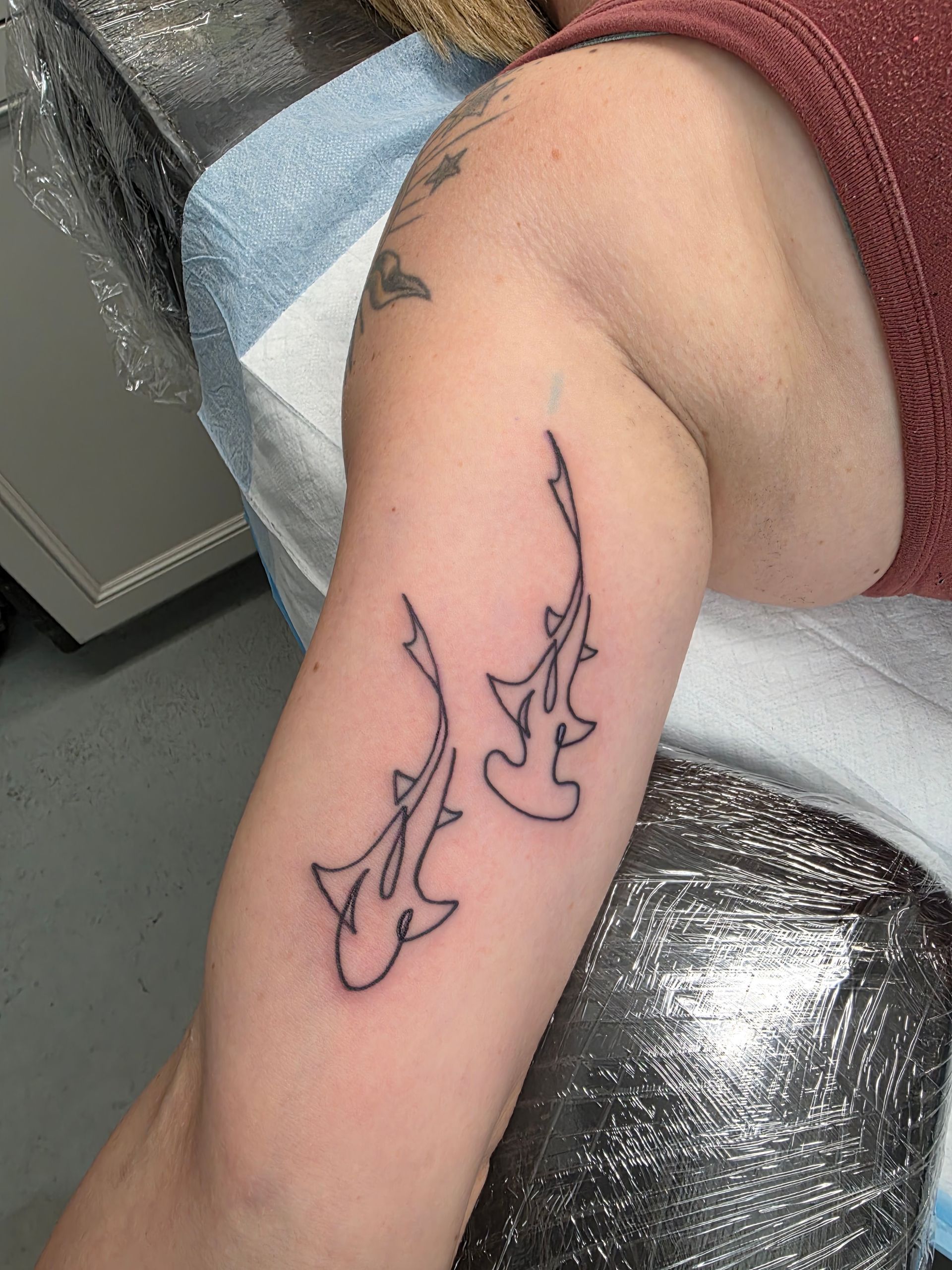 Two hammerhead shark outline tattoos on a person's upper arm.